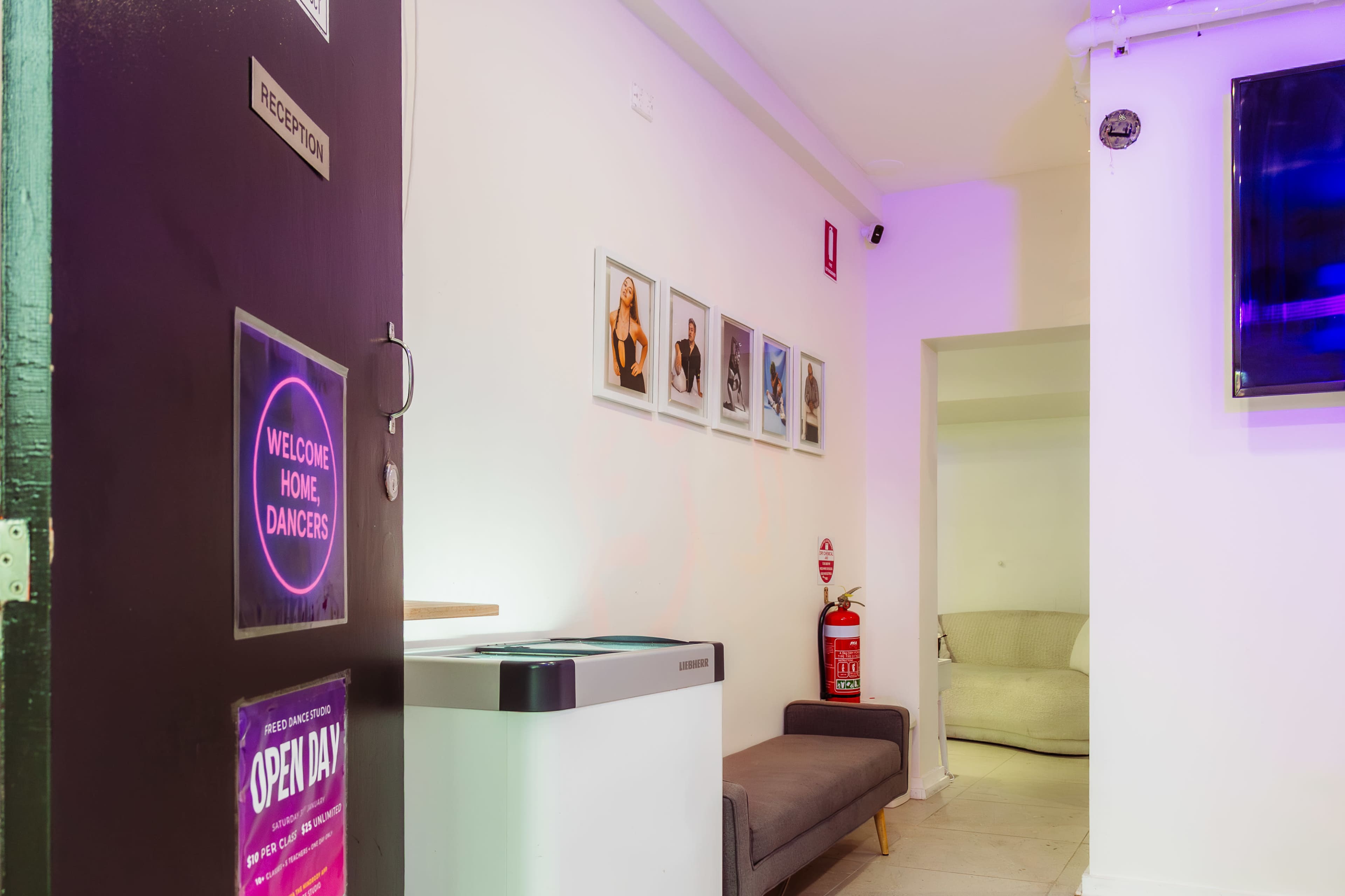 The image shows a reception area with a welcoming sign, framed photographs on the wall, and a couch in a well-lit, modern space.