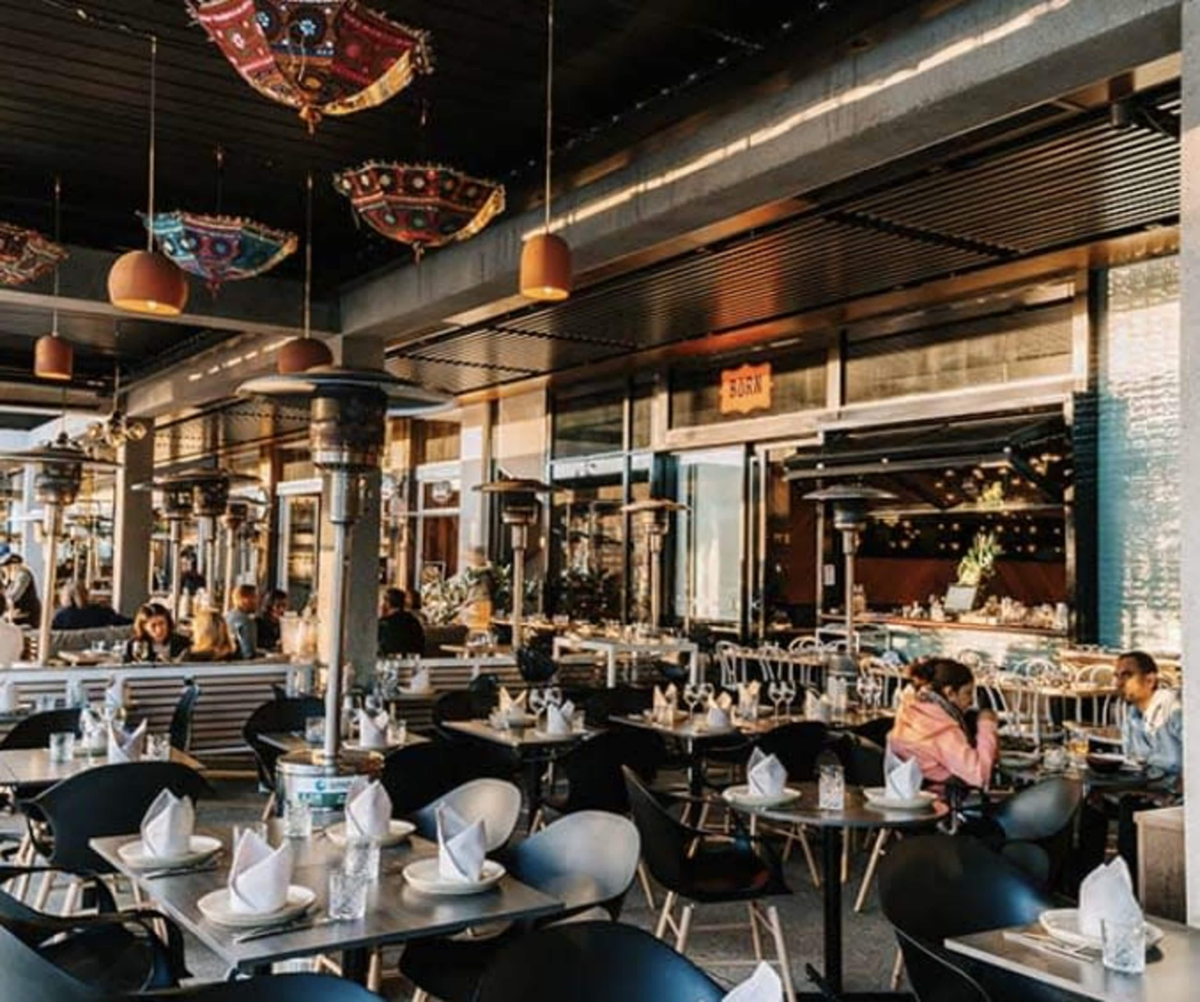 A modern restaurant interior with multiple tables set for dining and decorative lighting overhead.