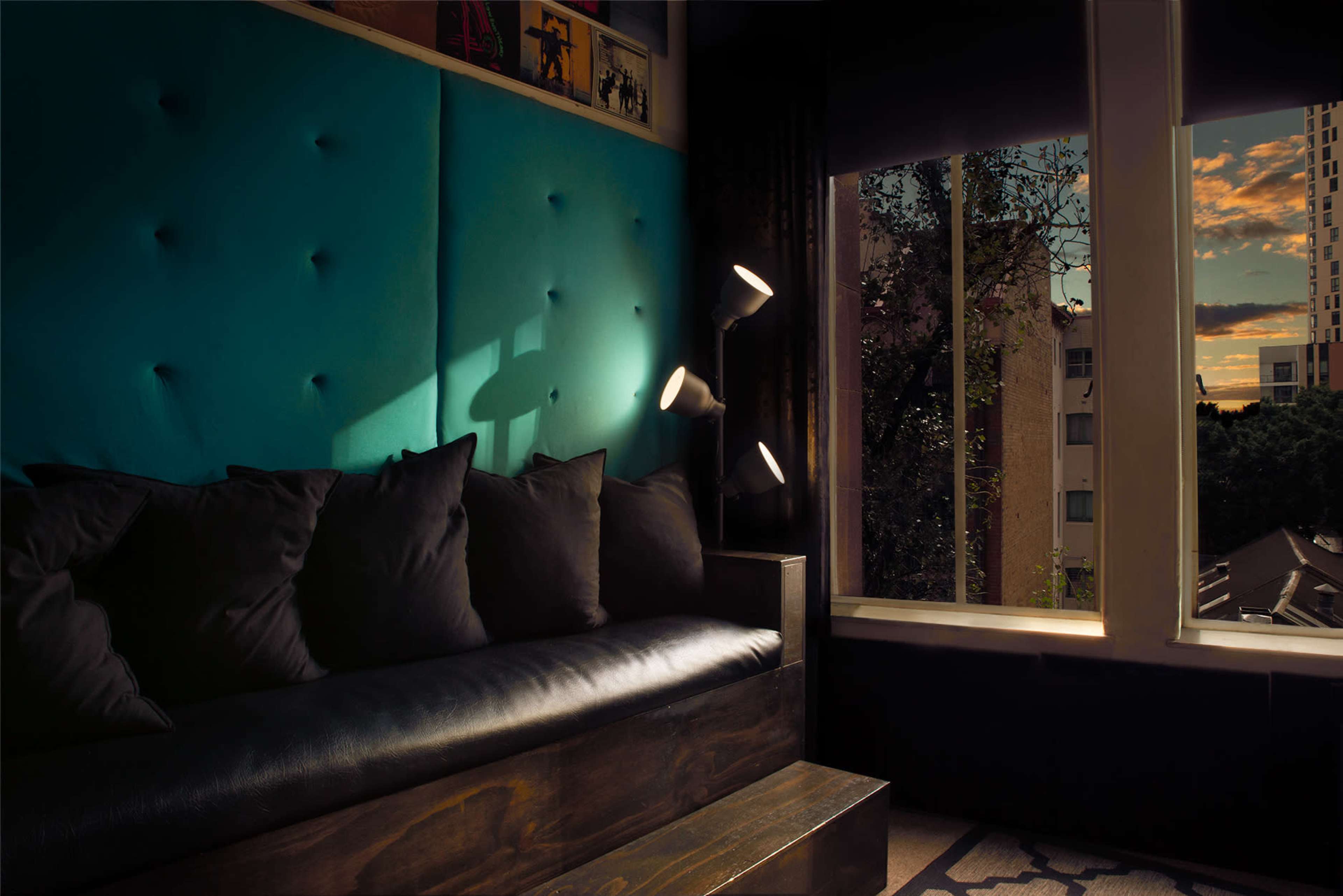 The scene features a dark couch with cushions against a bright blue wall, illuminated by a floor lamp, with a view of a cityscape through the window.