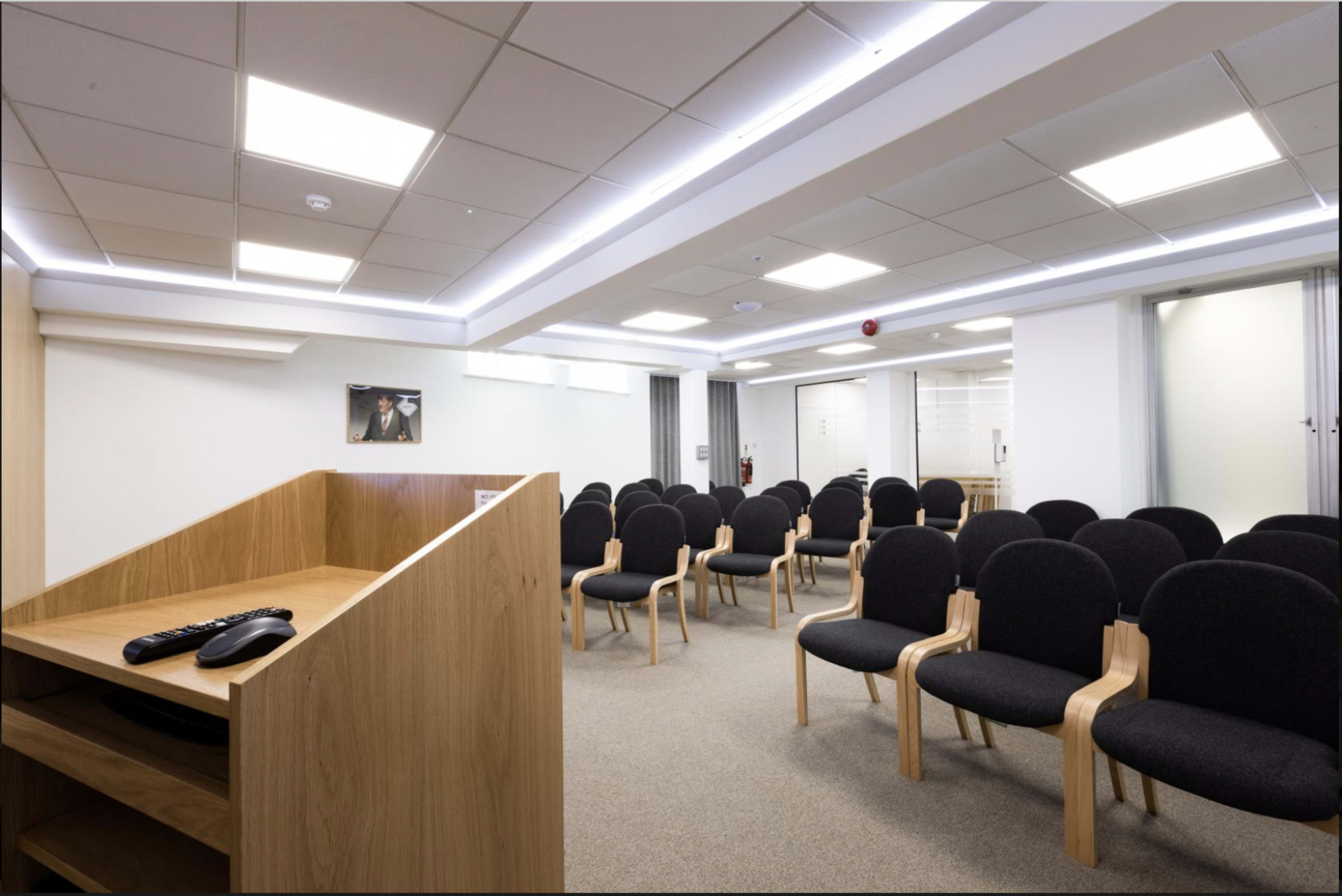 A modern meeting room arranged with black chairs facing a wooden podium at the front.