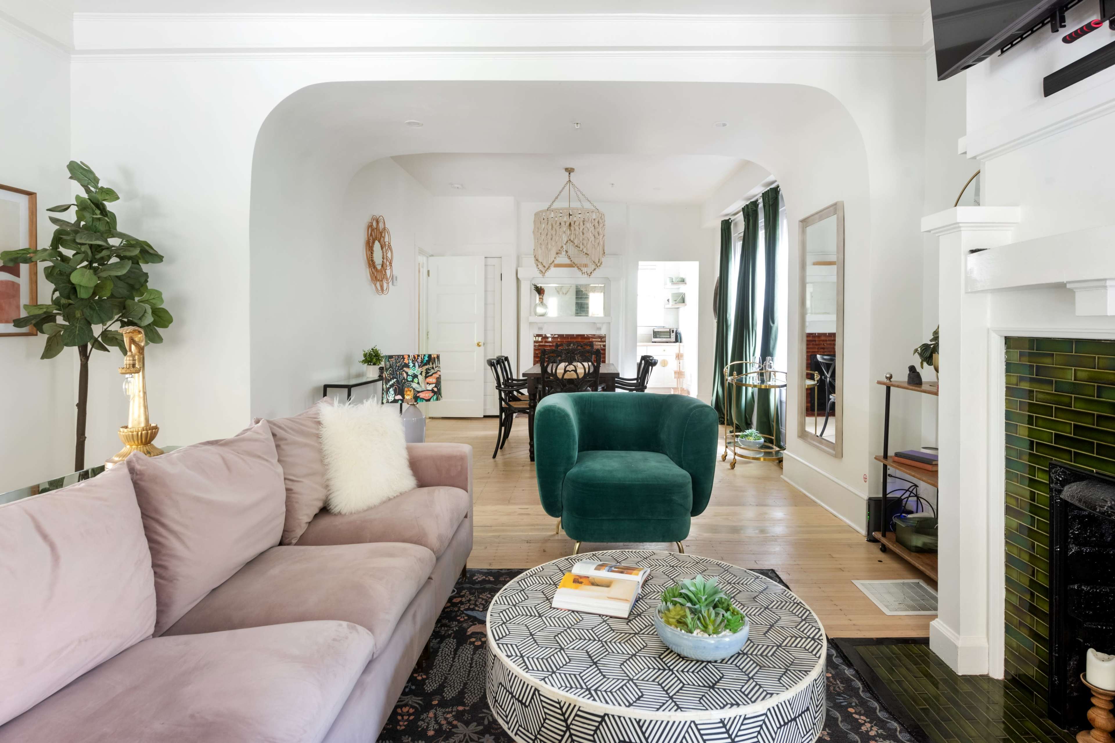 The image features a modern living room with a pastel-colored sofa and a green armchair, leading to an adjacent dining area visible through an archway.