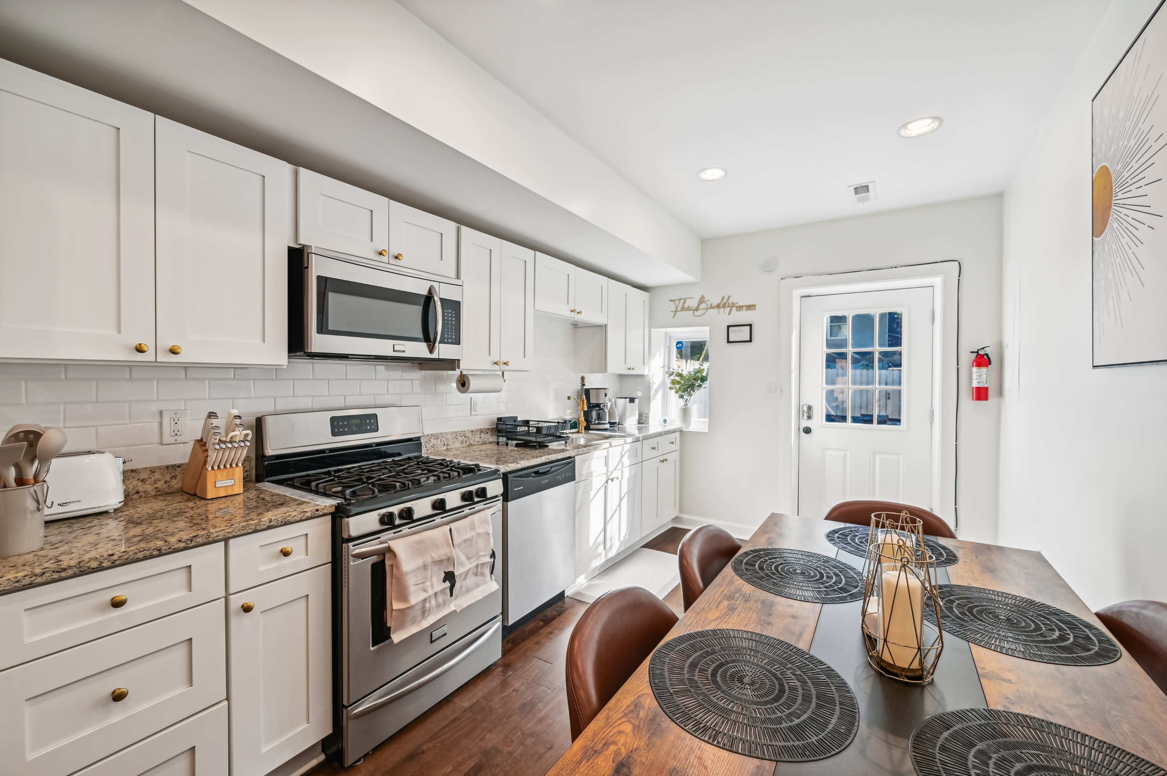 The image shows a modern kitchen with white cabinets, stainless steel appliances, and a wooden dining table set with circular placemats.