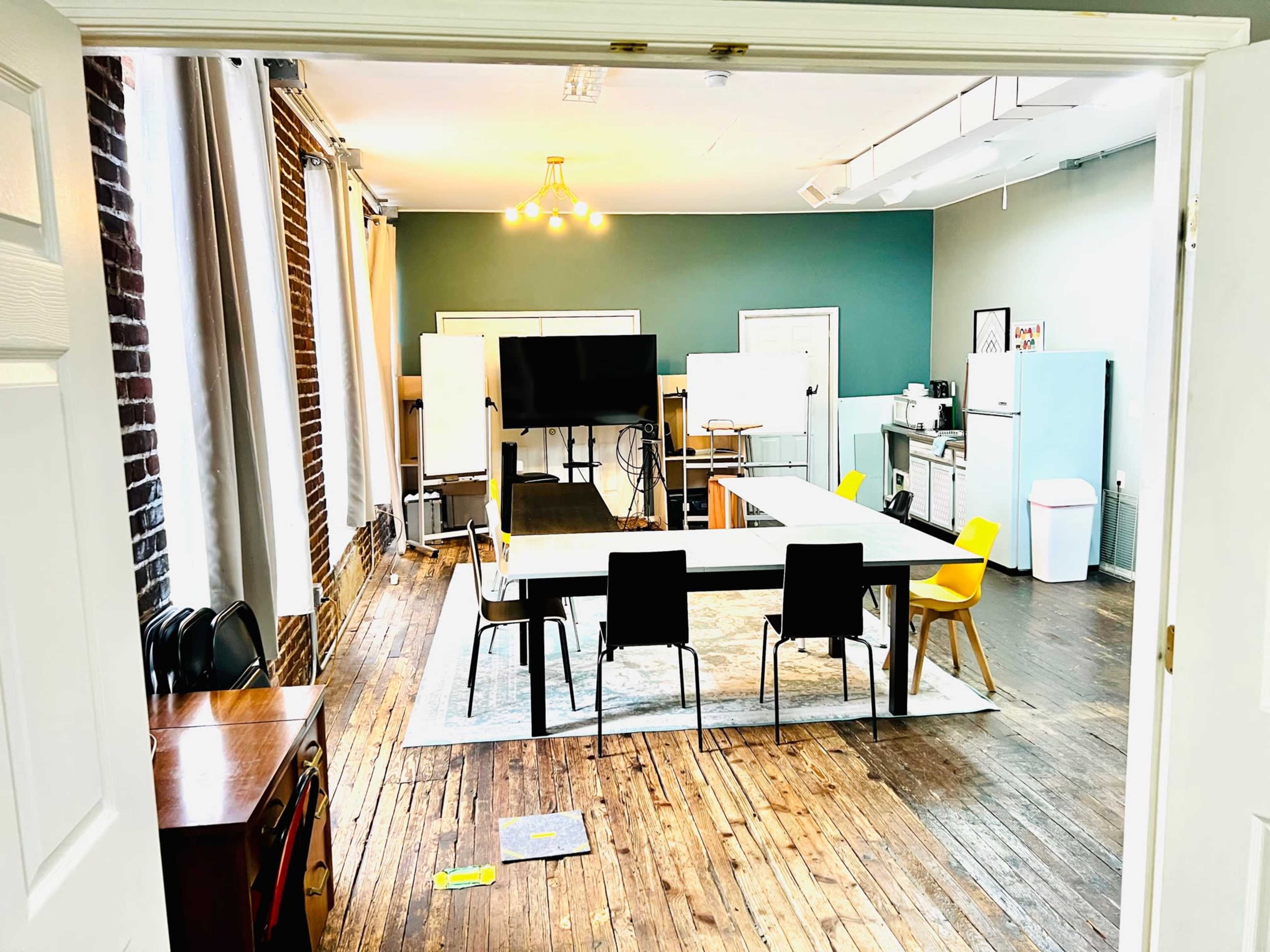 A brightly lit, modern meeting room with a long table, chairs, whiteboards, and a kitchenette in the background.
