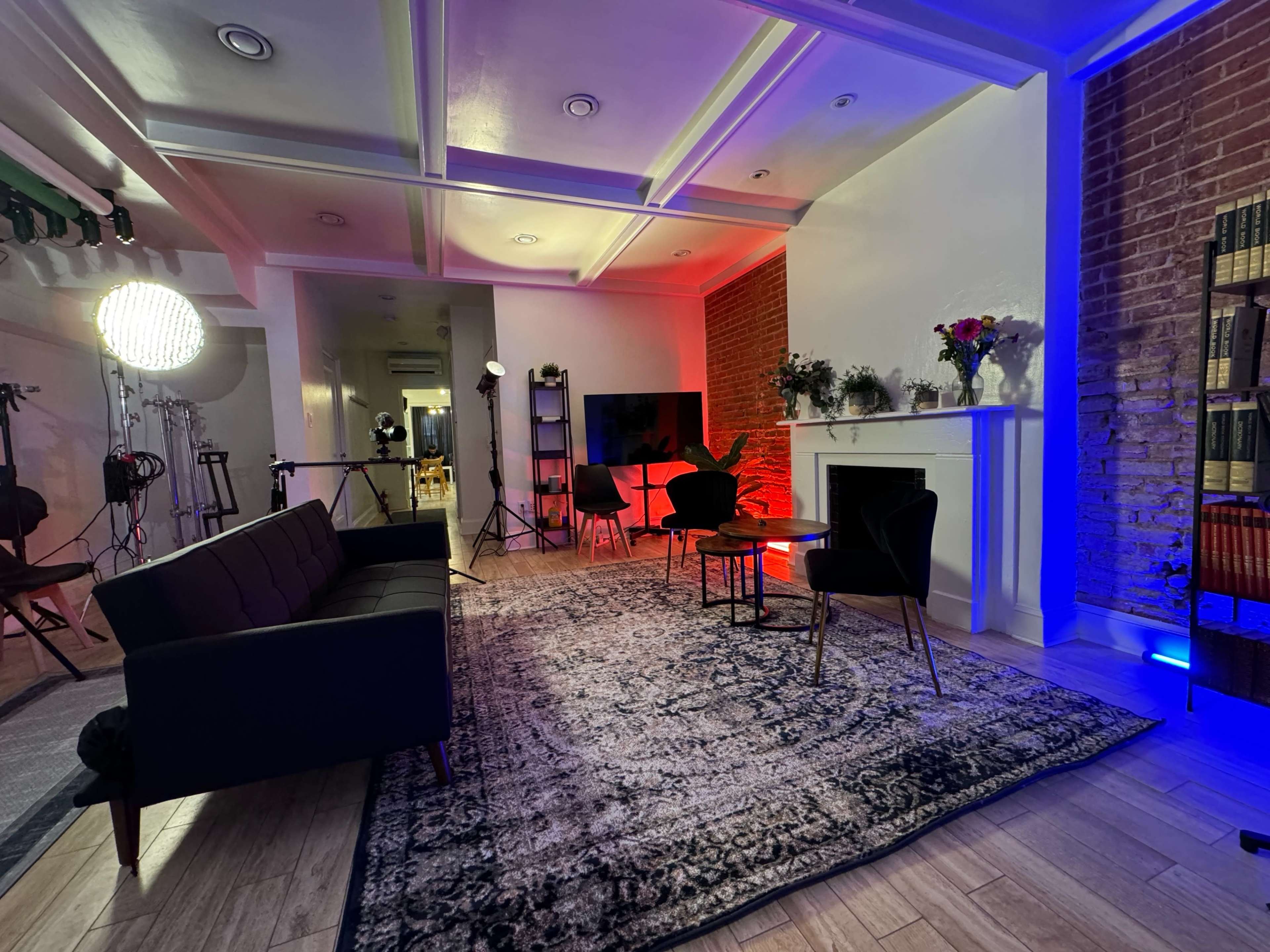 The scene features a modern interior setup with a sofa, decorative chairs, a large television, and a fireplace, illuminated by various colored lights.