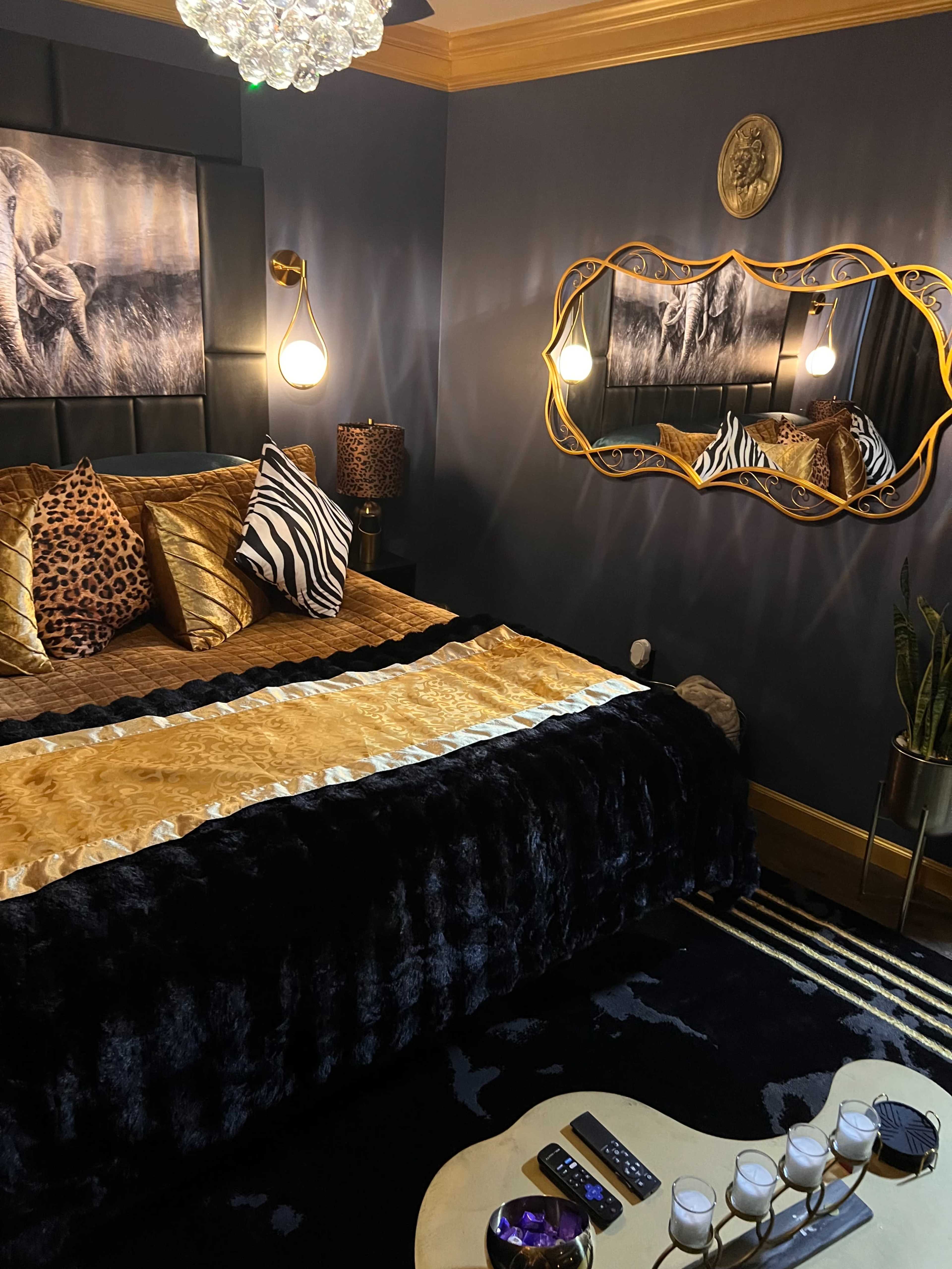 The image showcases a stylish bedroom featuring a dark color scheme, a large bed with decorative pillows, a statement mirror, and a decorative rug.