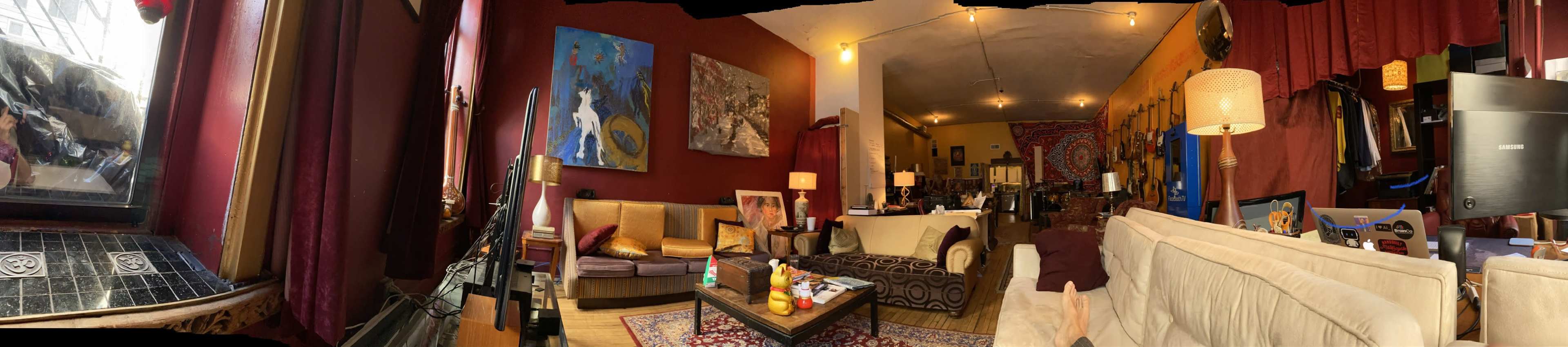 A spacious, artistically decorated living area with multiple seating arrangements, large artworks on the walls, and various items scattered throughout.
