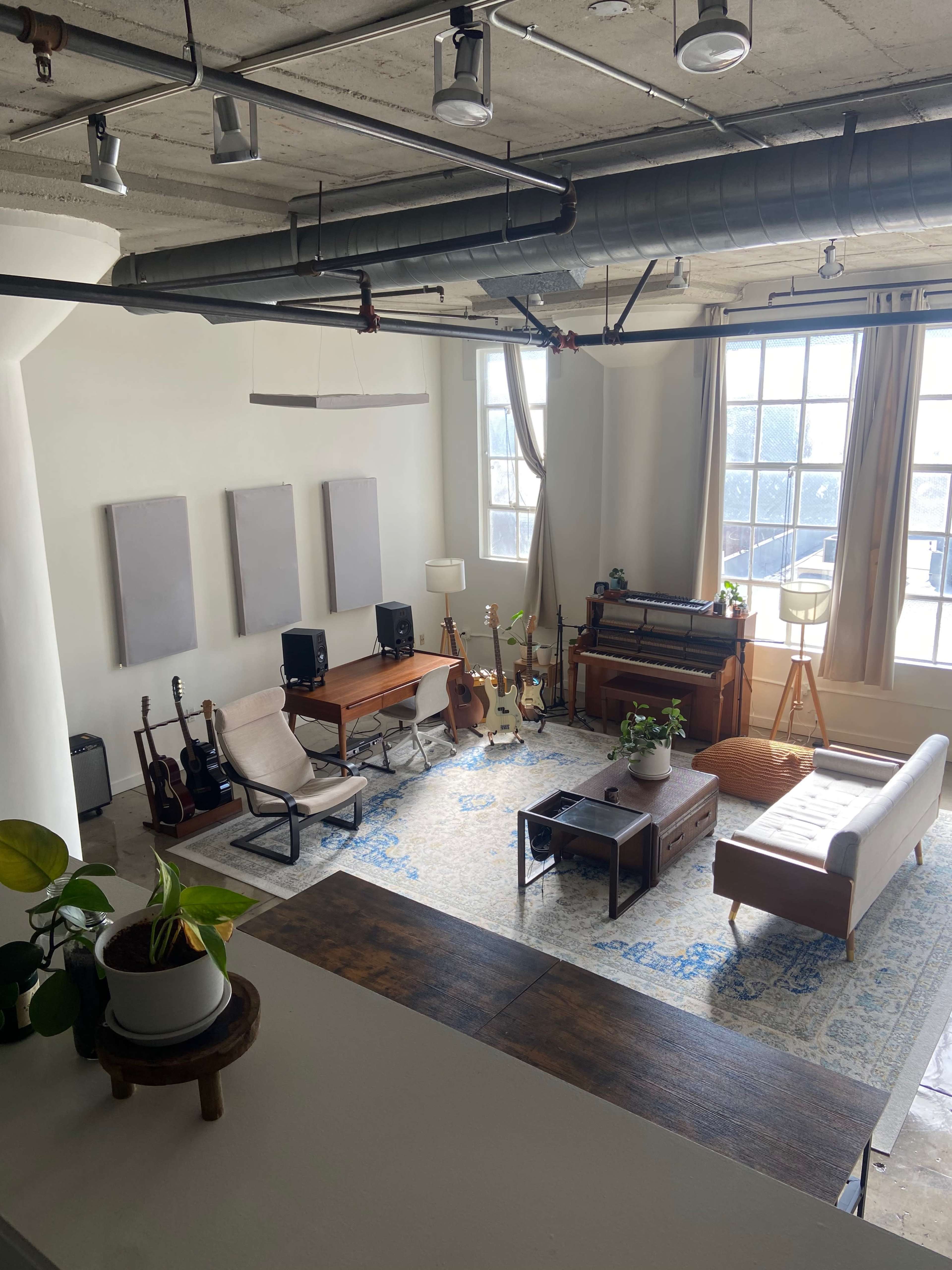 The image shows a spacious living area with musical instruments, a sofa, and large windows allowing natural light to fill the room.