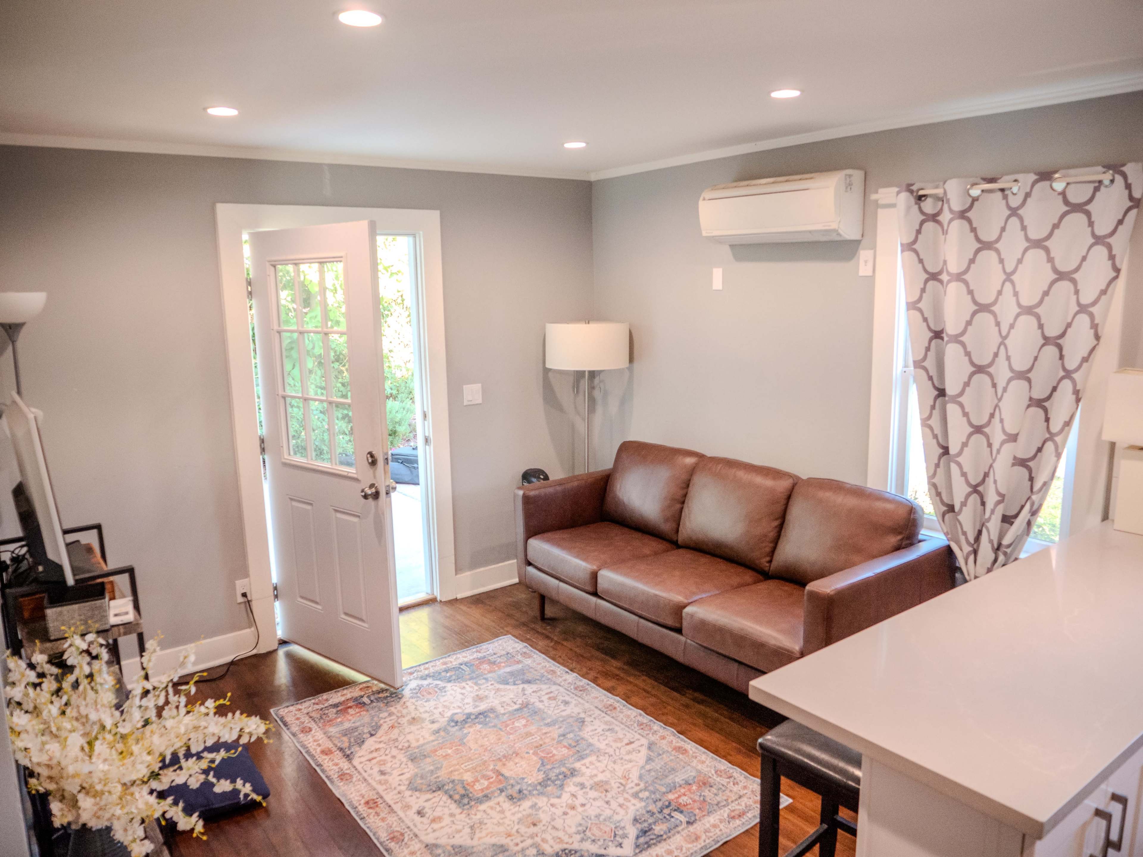 A living room with a brown leather sofa, a door leading outside, and a patterned curtain over a window.