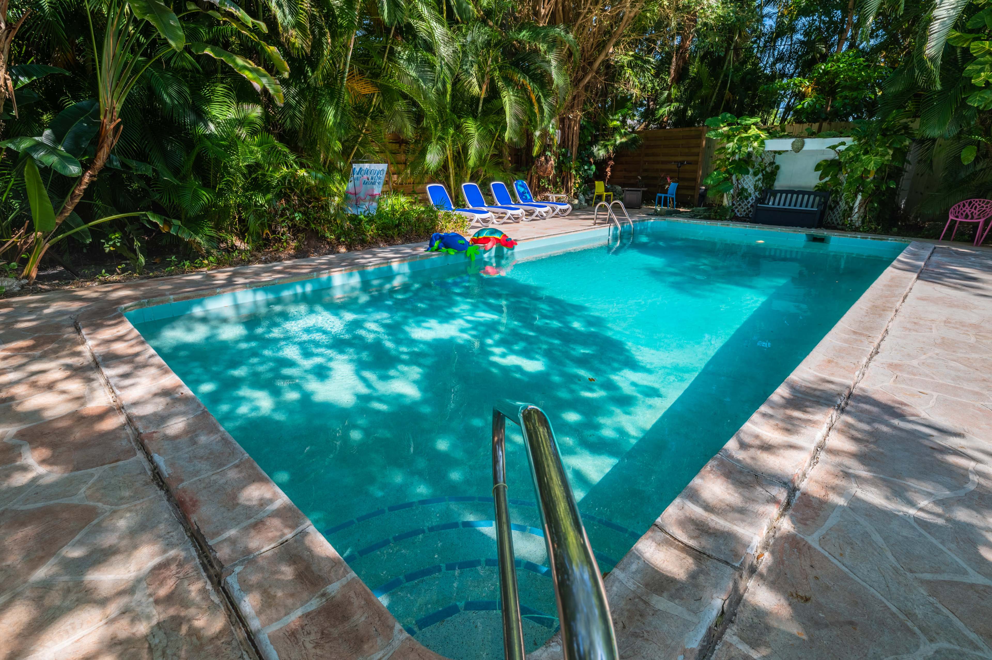 A clear swimming pool surrounded by tropical greenery and lounge chairs.