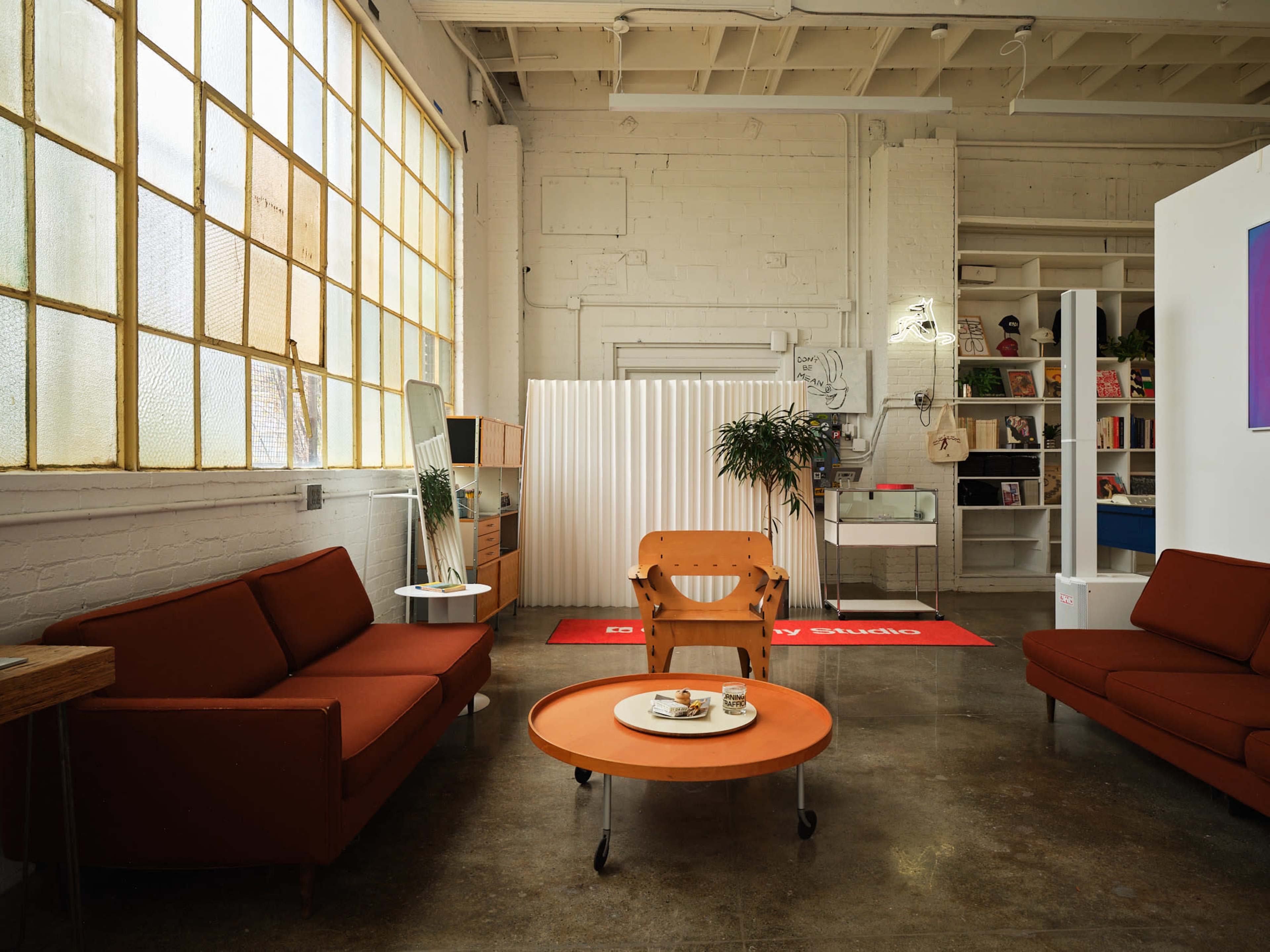 The scene depicts a modern, well-lit living space featuring two red sofas, a round orange coffee table with snacks, and a partitioned area in the background.