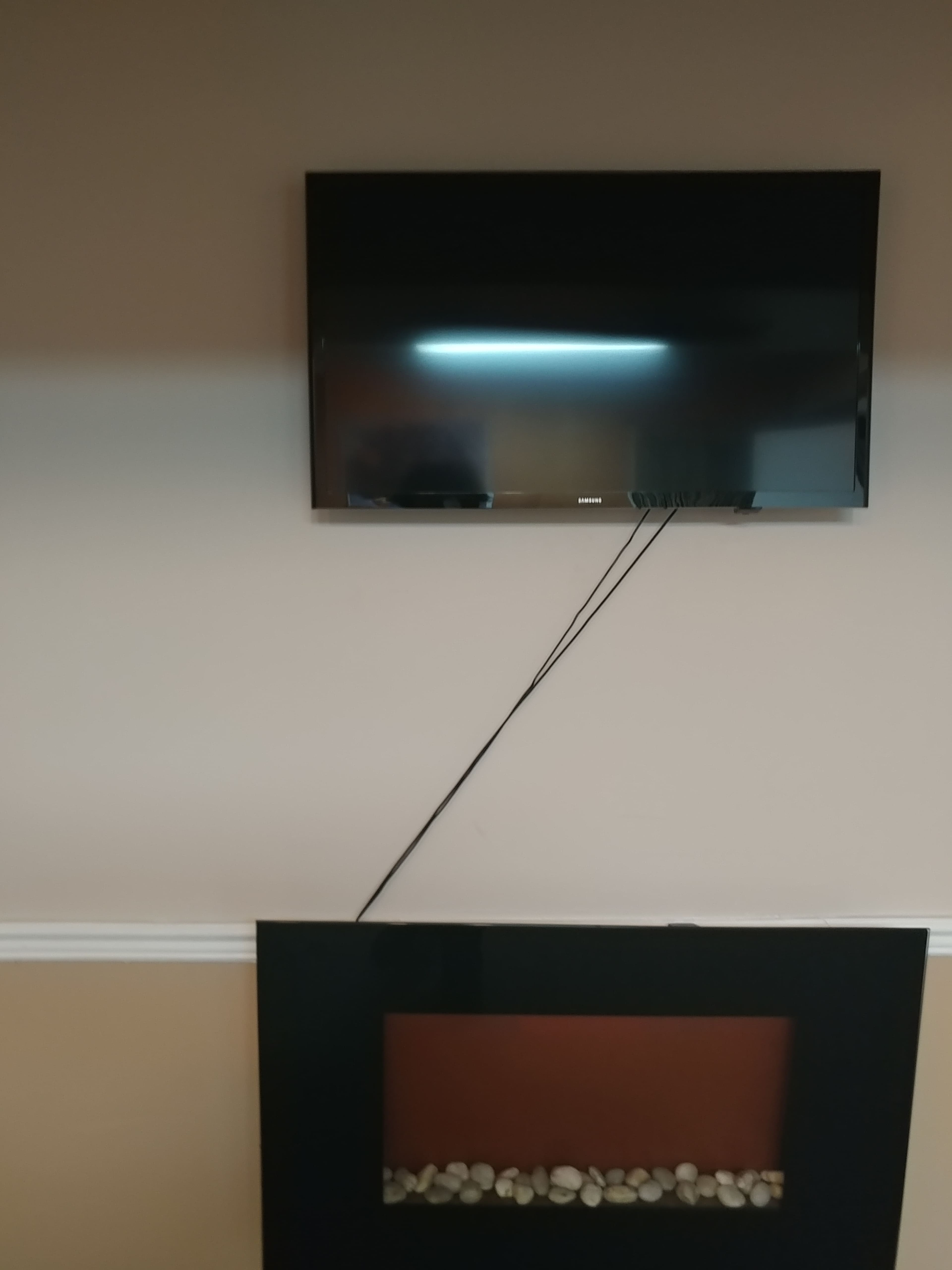 A flat-screen television is mounted on a beige wall above a black fireplace with decorative stones.