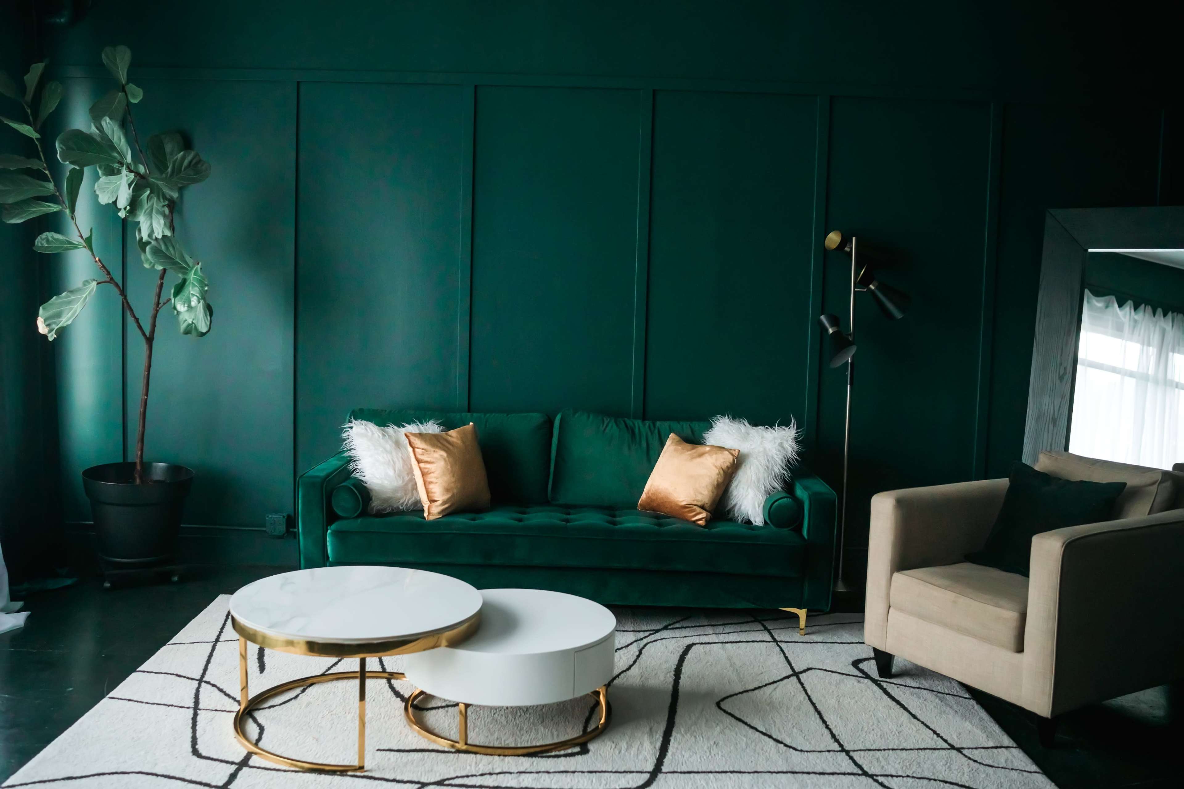The image features a stylish living room with a dark green wall, a green sofa adorned with pillows, a light-colored circular coffee table, and a beige armchair.