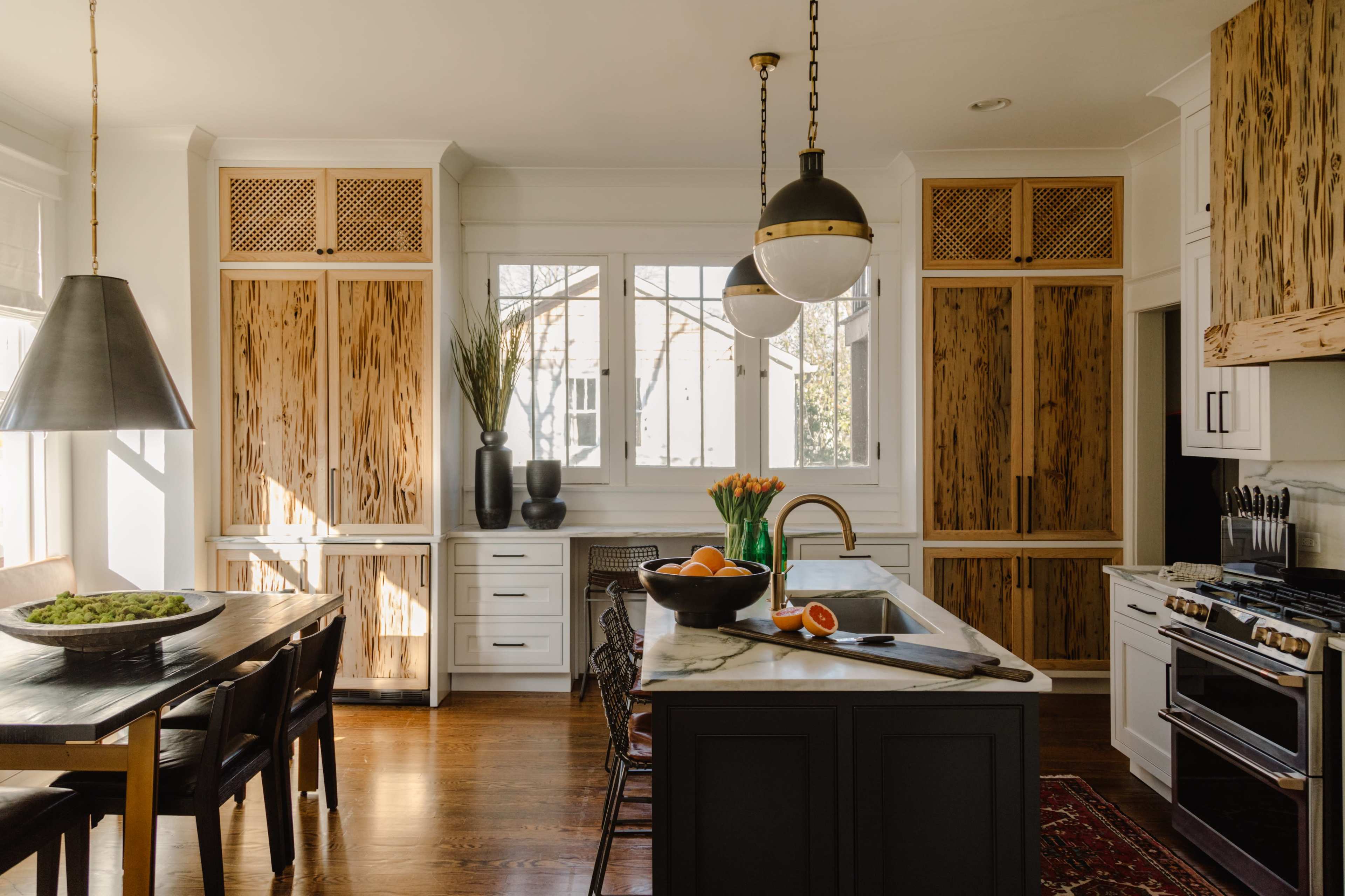 The kitchen features a central island with a marble countertop, wooden cabinets, and a dining table with black chairs.