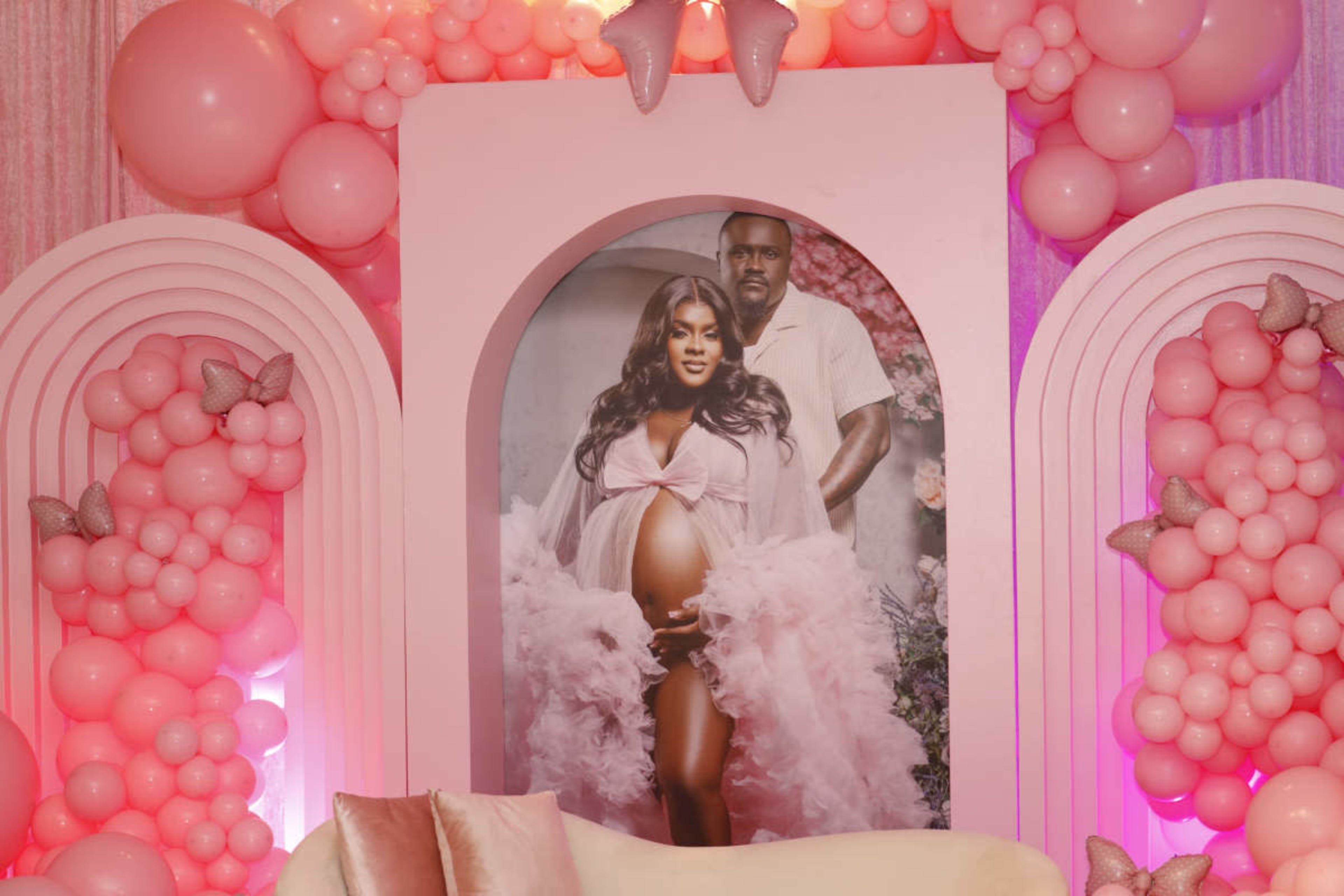 A large circular photo of a pregnant woman in a flowing pink dress is displayed against a backdrop adorned with pink balloons and decorative arches.