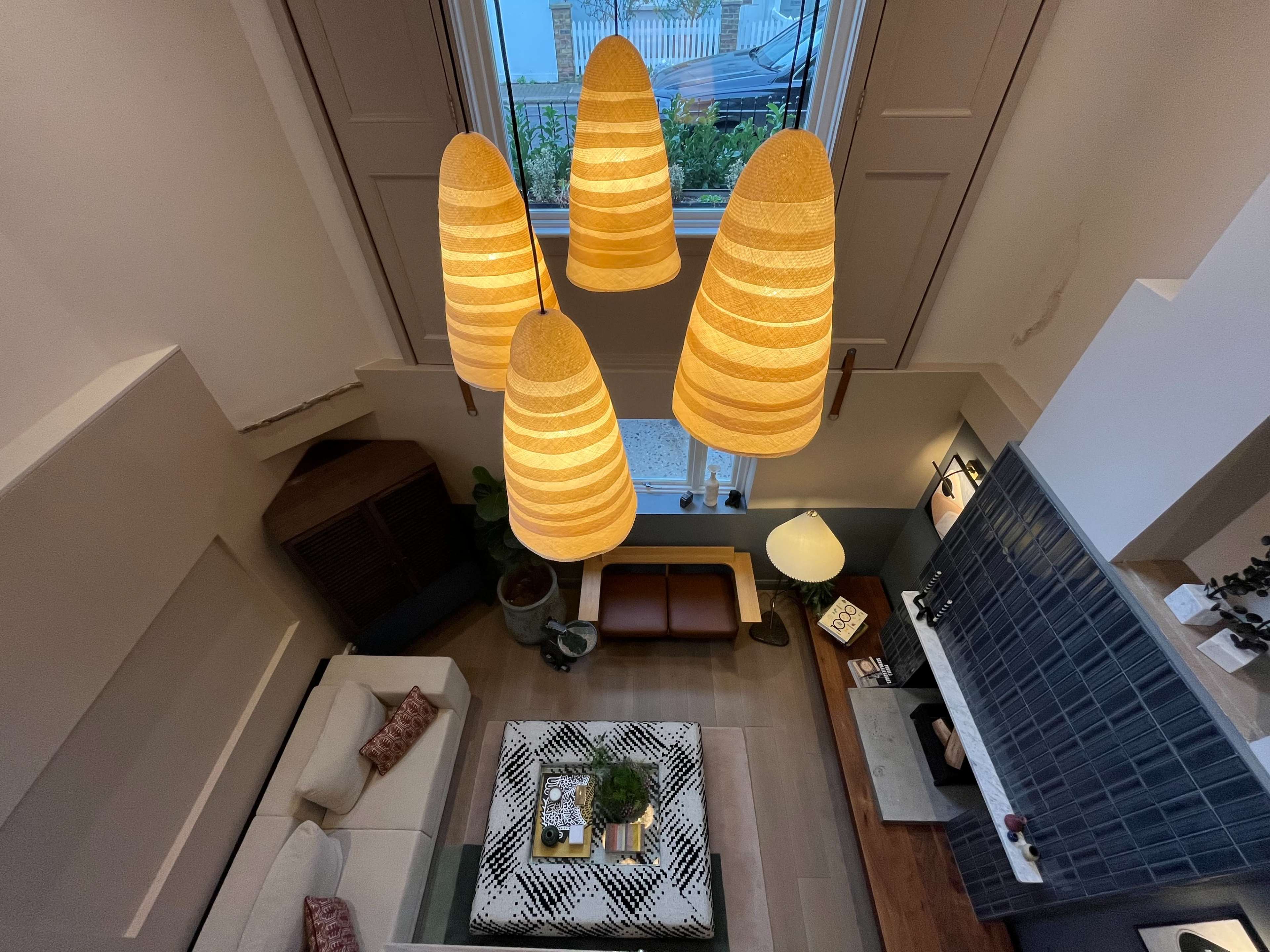The image shows a well-lit living room with modern furniture, a large coffee table, and pendant lighting hanging from the ceiling.