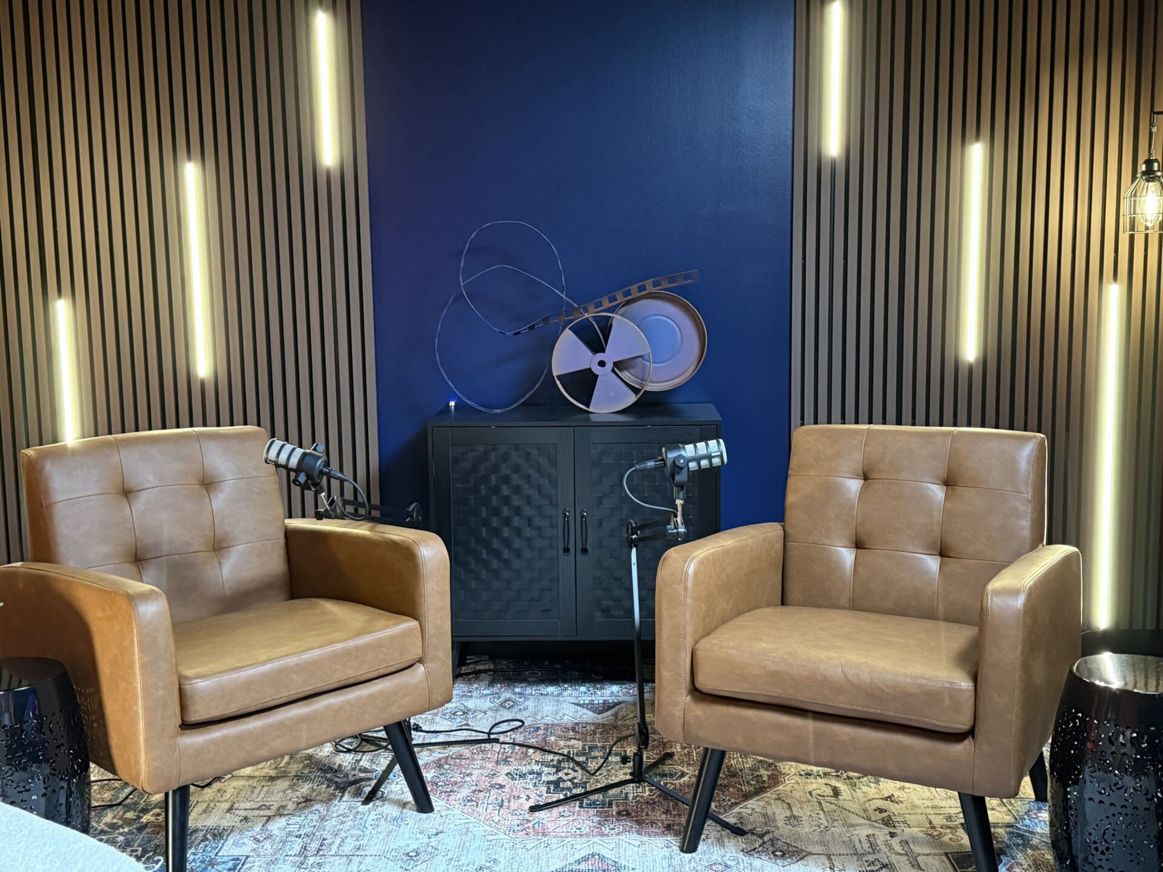 The image shows two brown leather armchairs positioned in a recording studio with wooden paneling and ambient lighting.