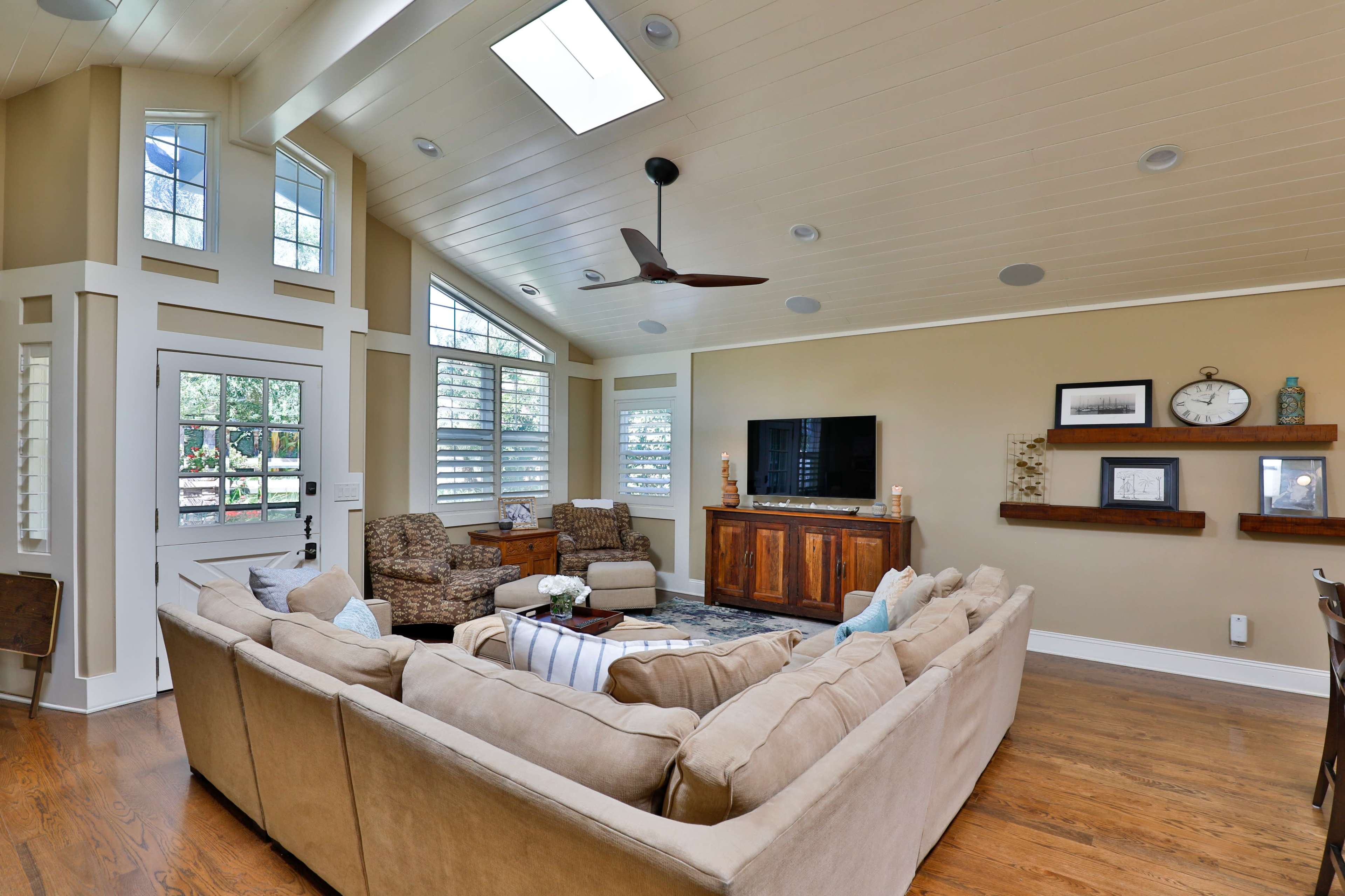 A spacious living room with a large sectional sofa, two armchairs, a wooden entertainment center, and decorative shelves against warm-toned walls.