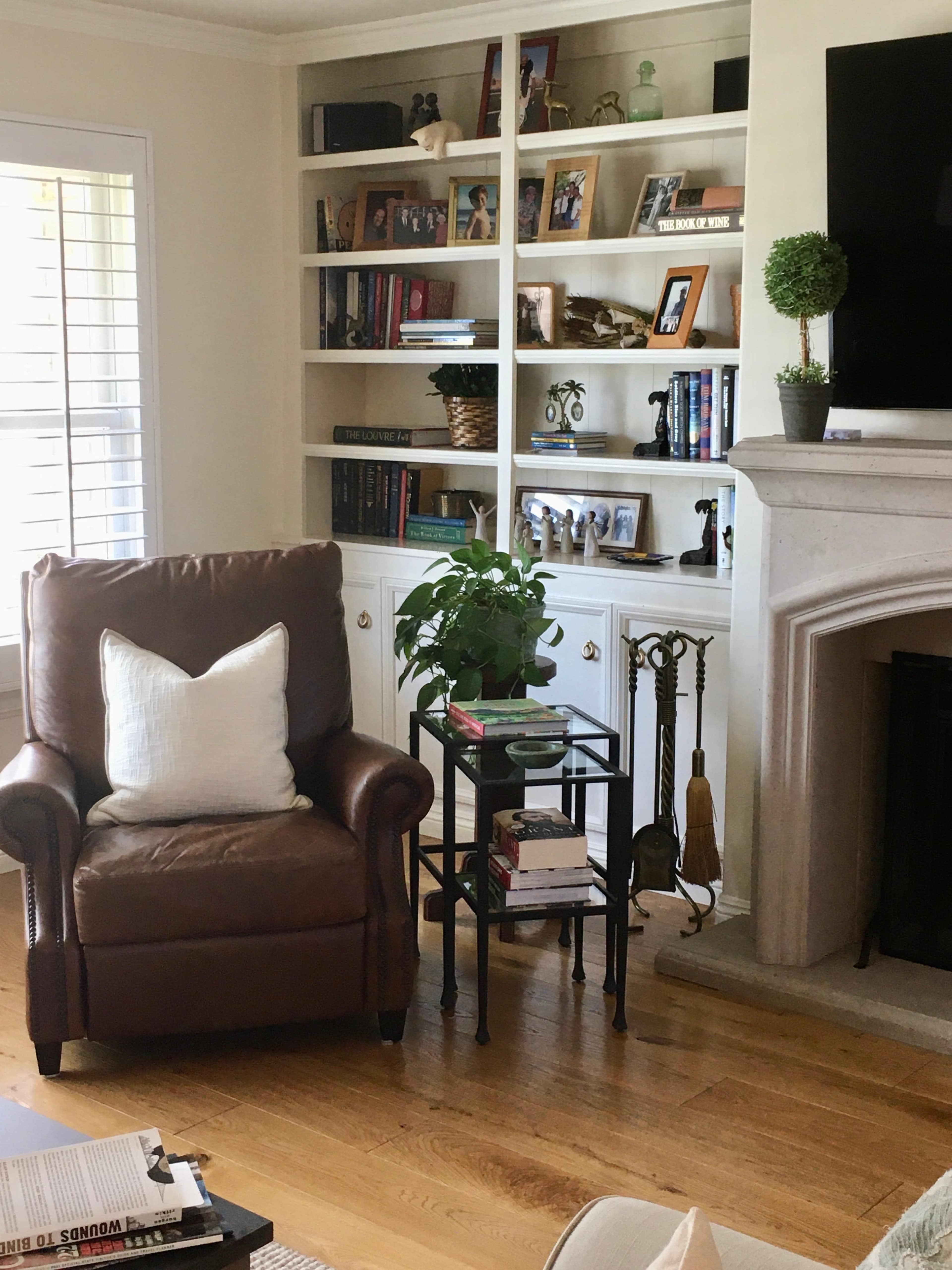 A brown leather armchair sits next to a small black side table and a bookshelf filled with books and decorative items.