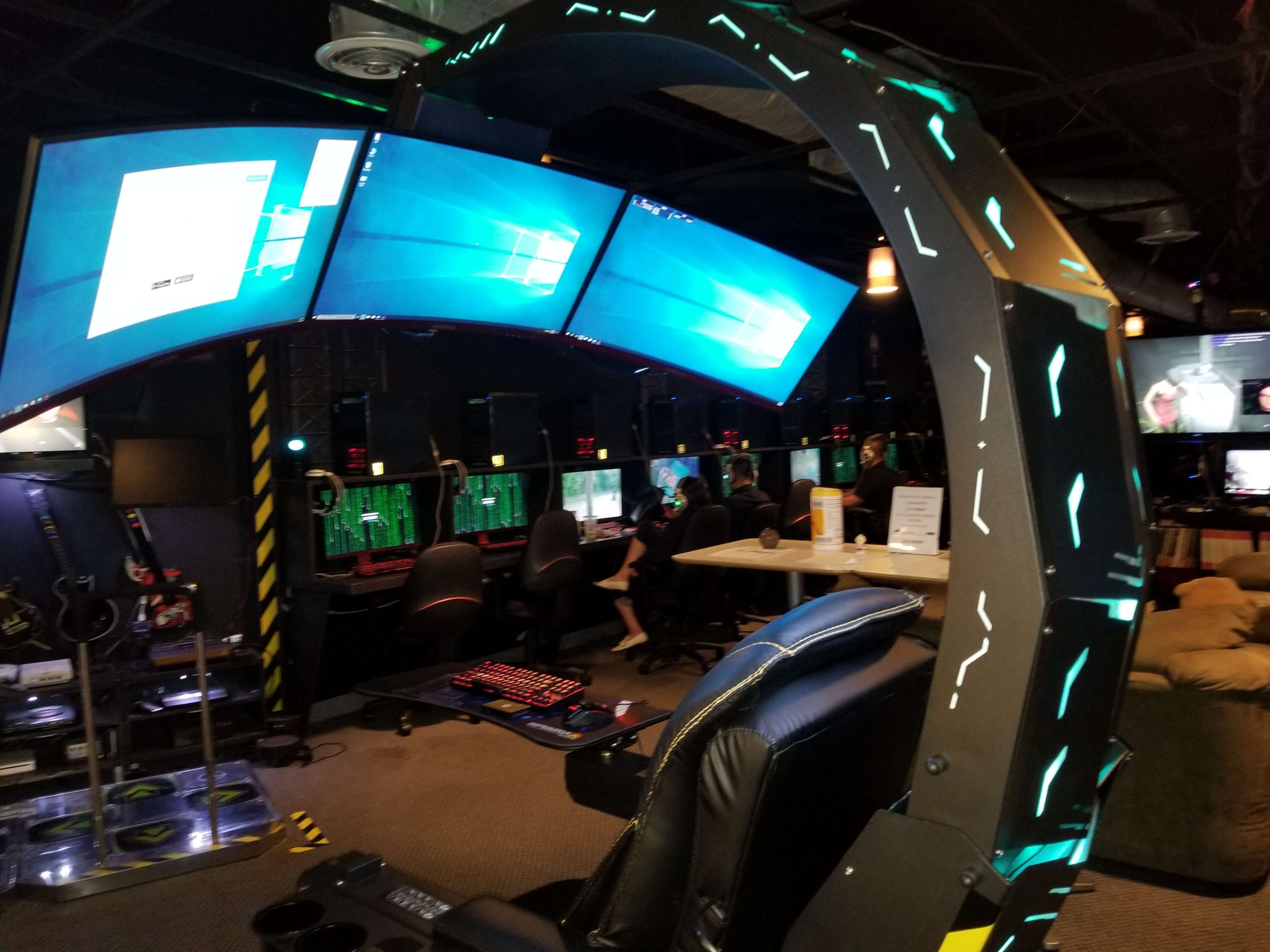 A gaming lounge featuring multiple computer stations with curved monitors, gaming chairs, and a futuristic design.