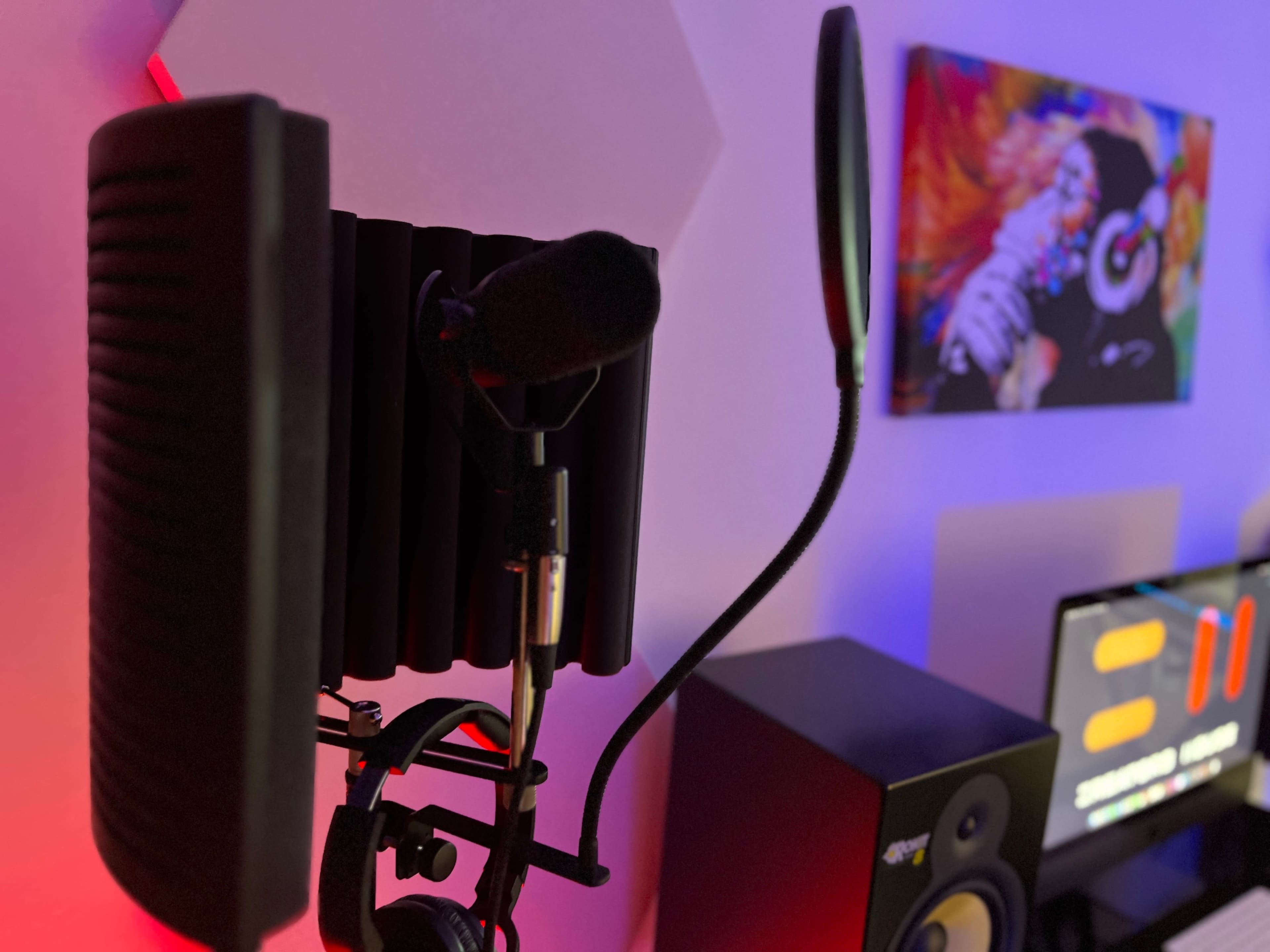 A microphone setup with a pop filter, colorful wall art in the background, and audio equipment visible on a desk.