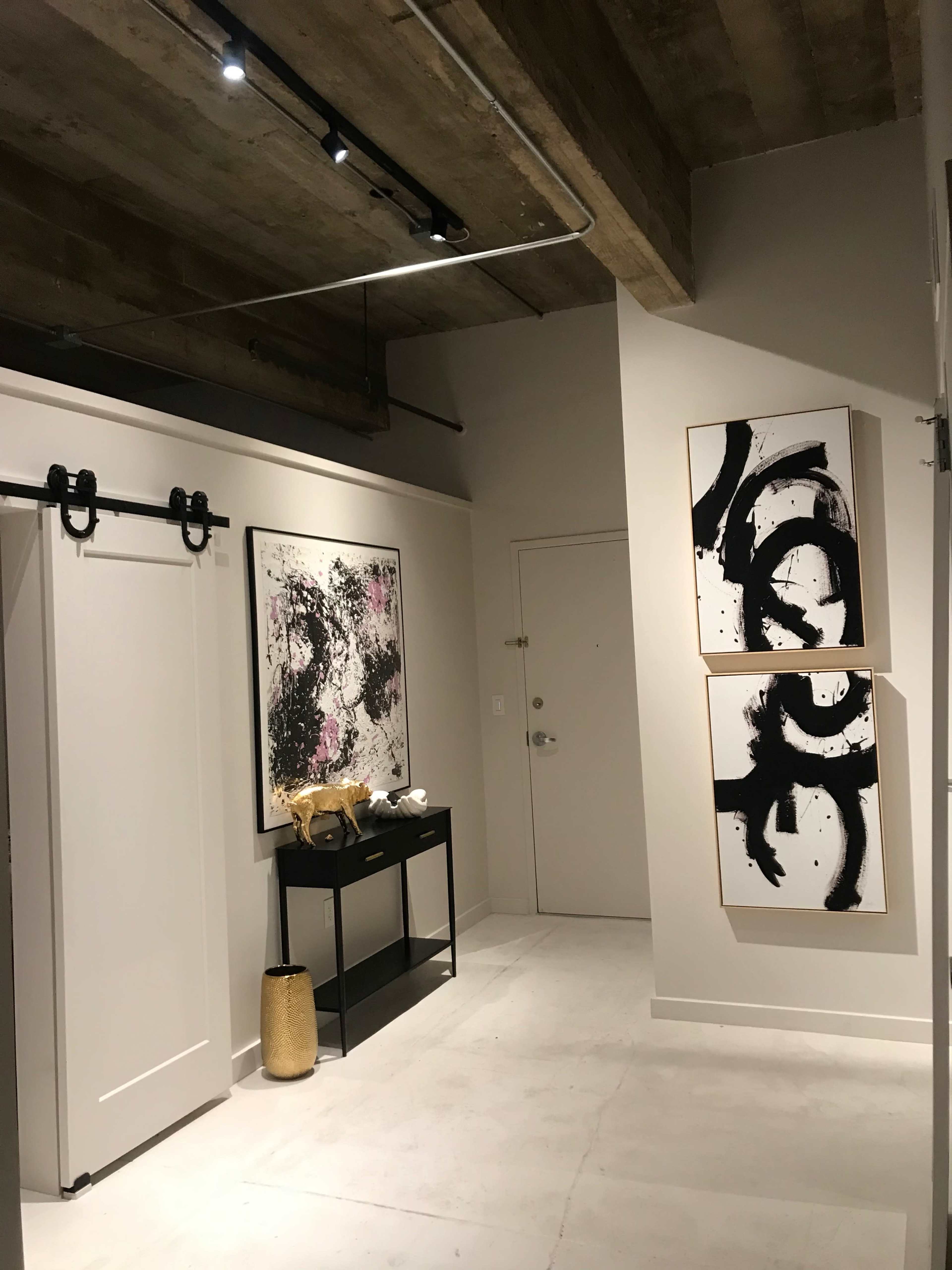 A modern hallway featuring a sliding barn door, abstract artwork on the walls, a black console table, and a decorative gold vase.