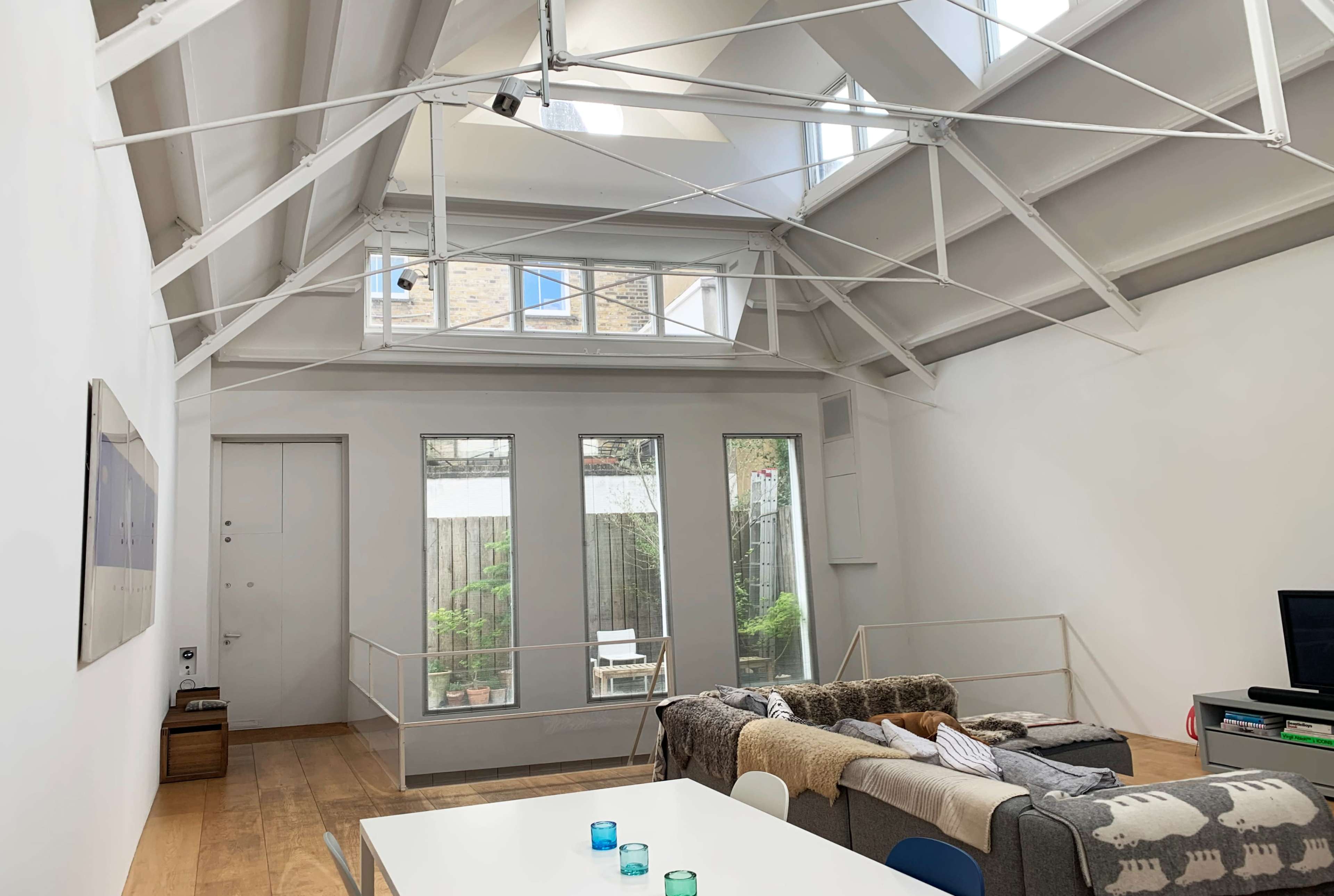The image shows a modern interior living space with a high ceiling, large windows, and a seating area that includes a couch and a coffee table.