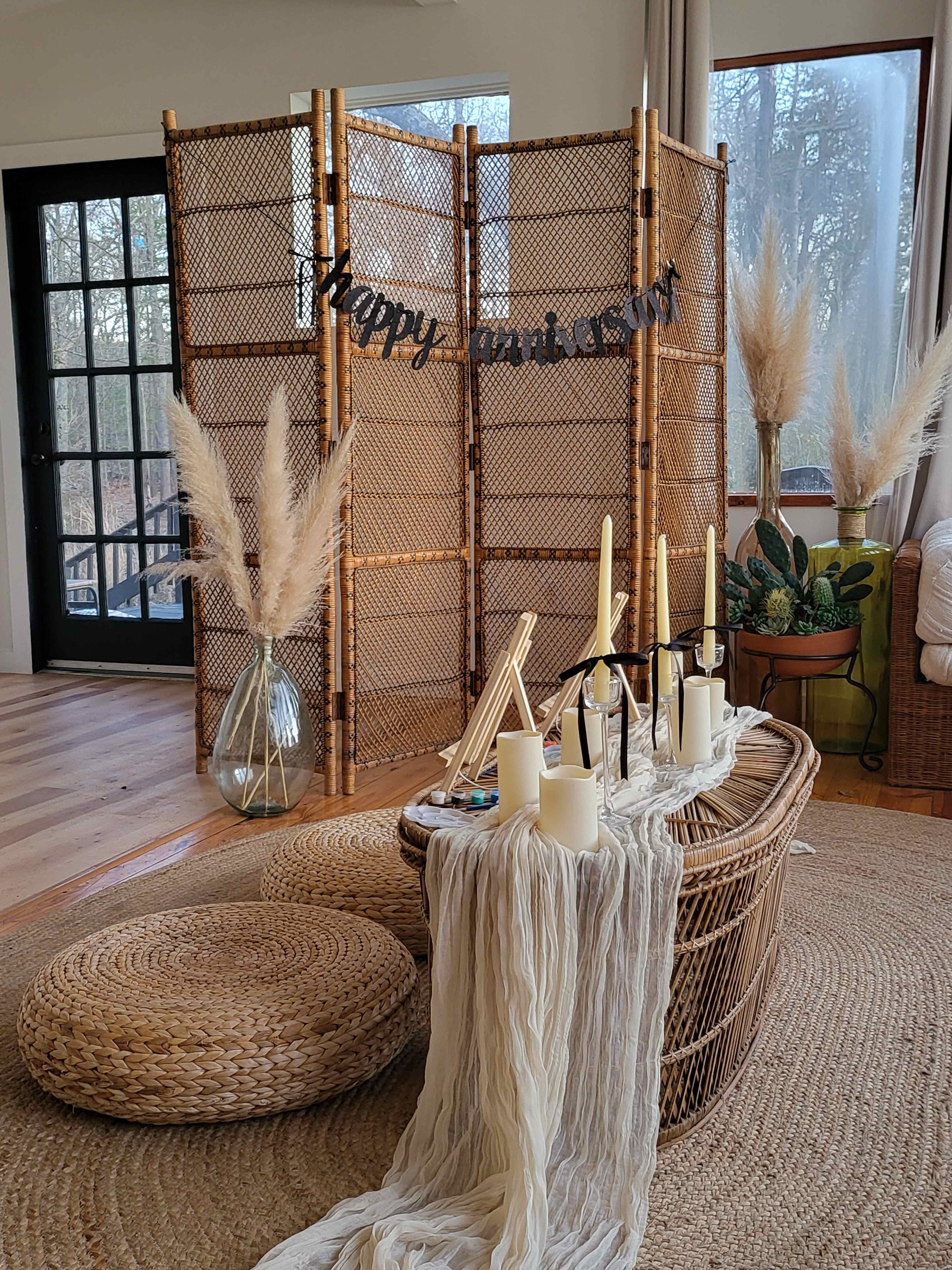 The image features a cozy interior with a bamboo room divider, decorative candles on a table, and pampas grass arrangements in vases.