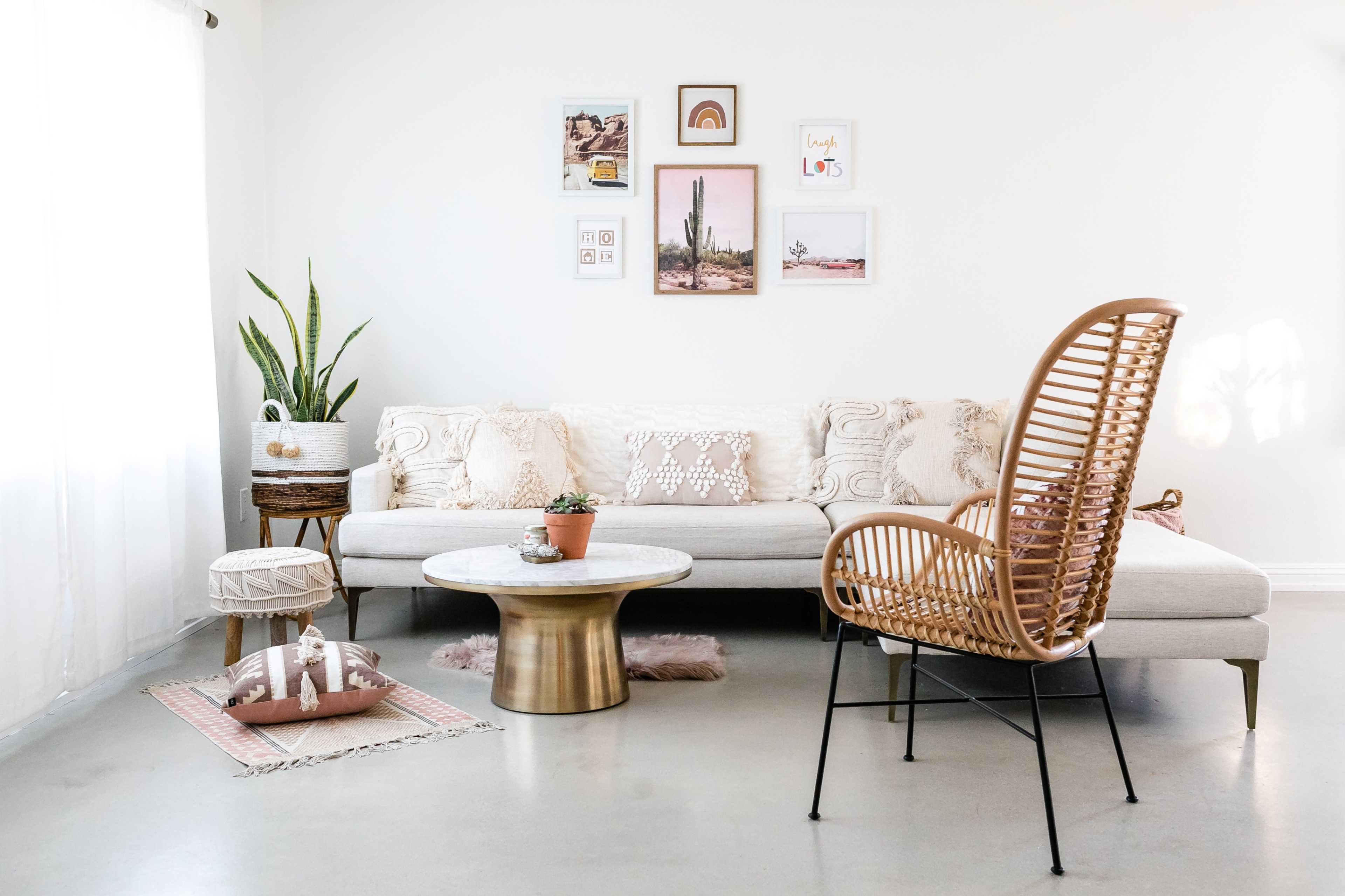 A modern living room features a sectional sofa with decorative pillows, a round coffee table, a rattan chair, and various plants and artwork on the walls.
