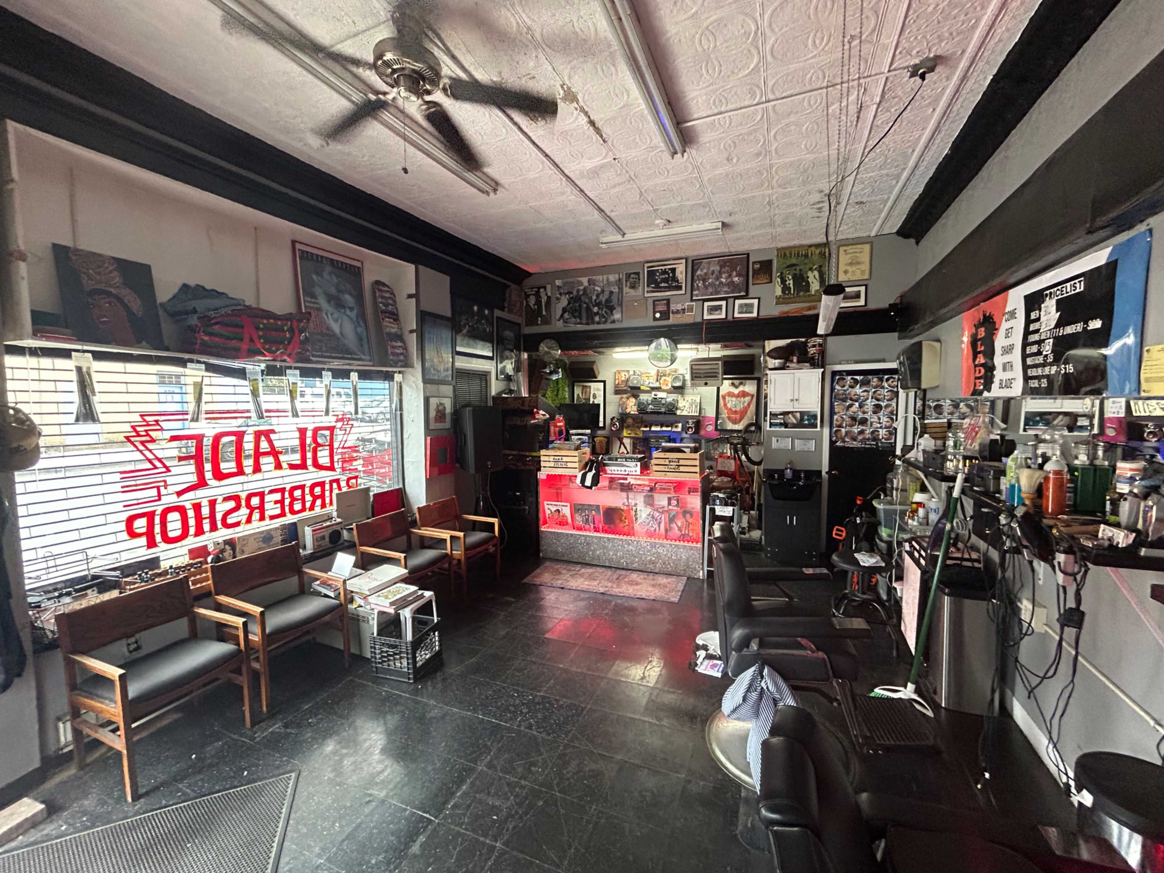 The image shows the interior of a barbershop with several styling chairs, vintage decorations, and a brightly lit reception area.