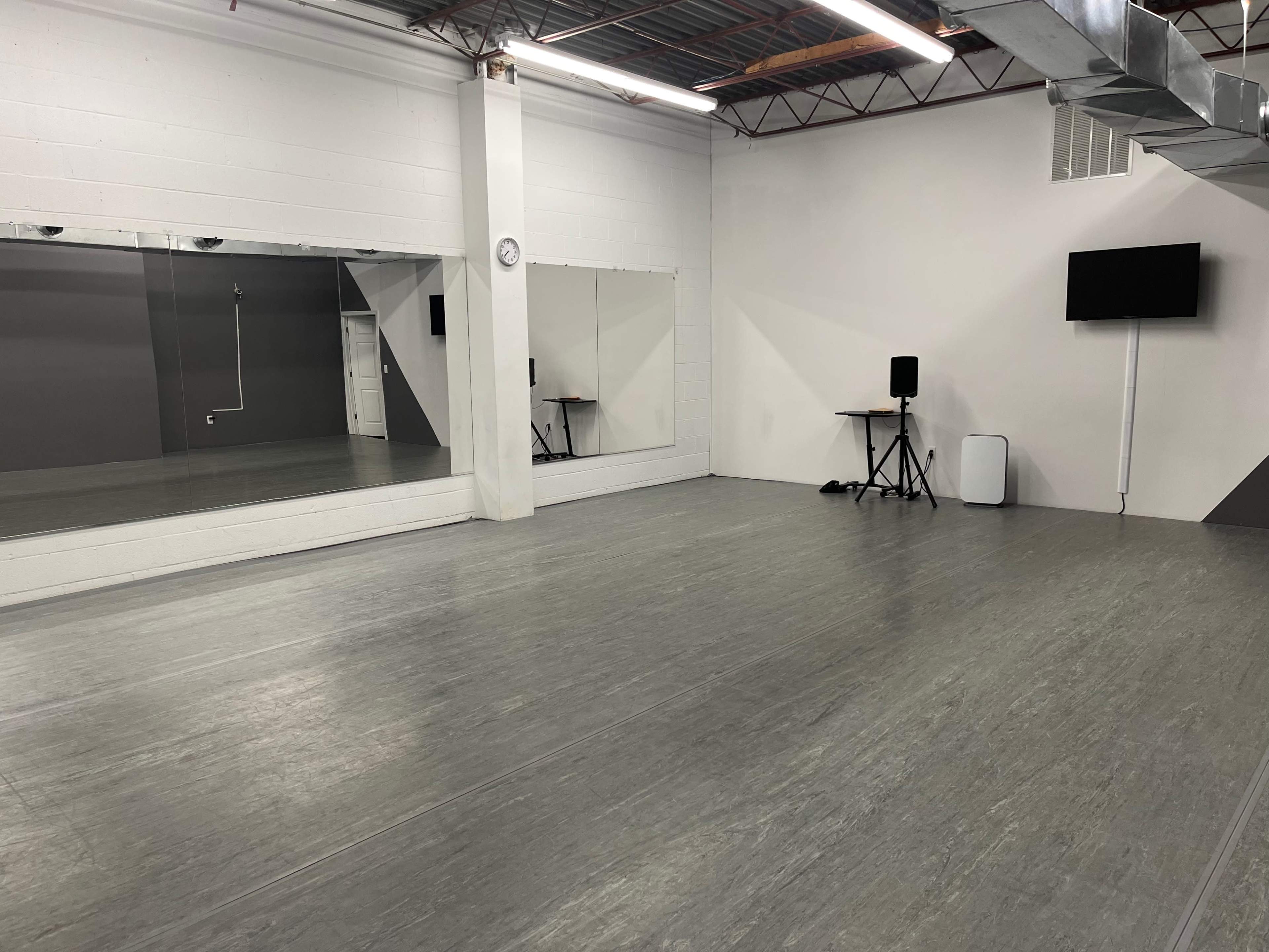 An empty dance studio featuring a large mirrored wall, a speaker setup, and a television mounted on the wall.