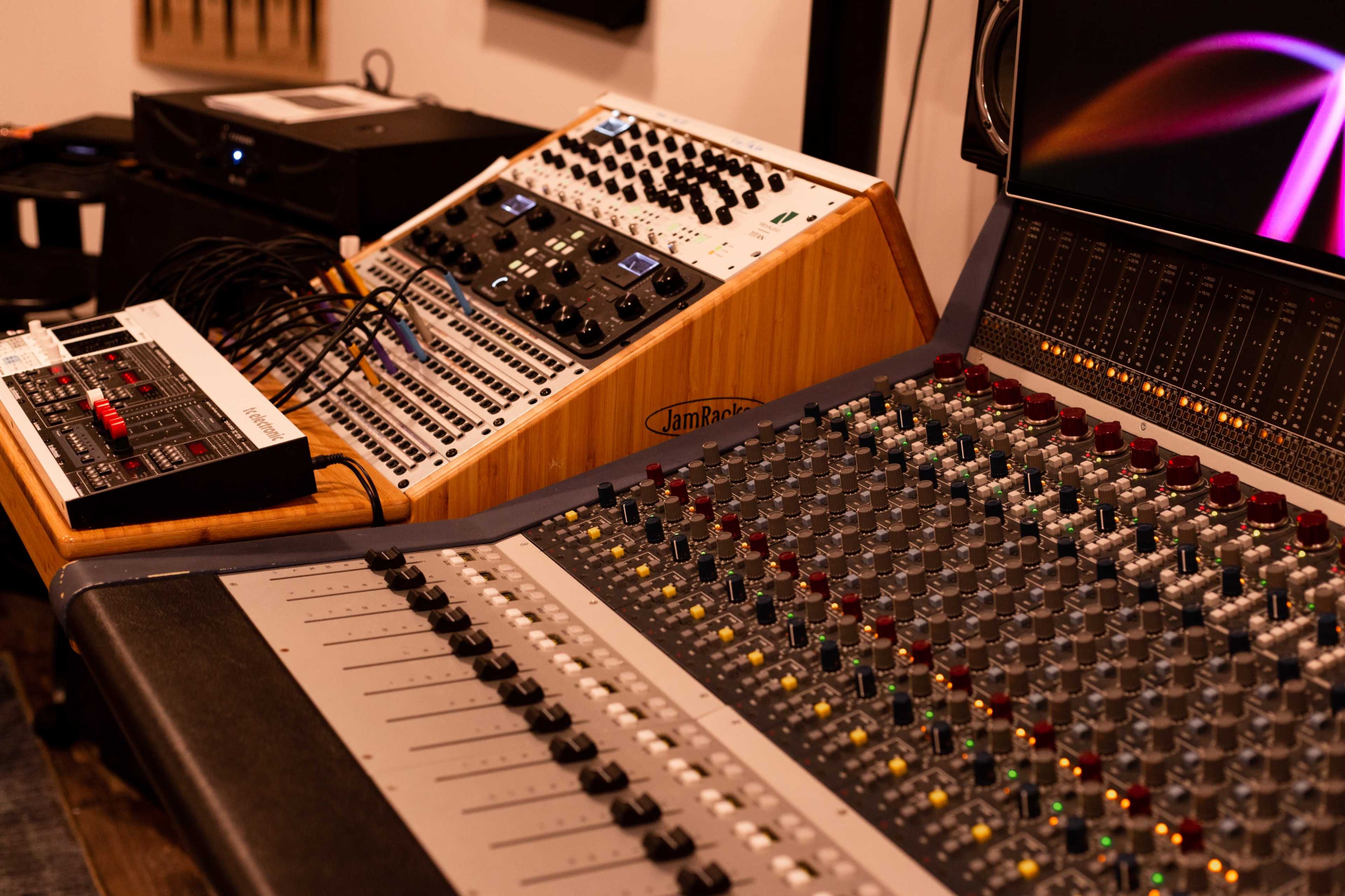 A music production setup featuring a large sound mixing console alongside various audio equipment and a computer screen.