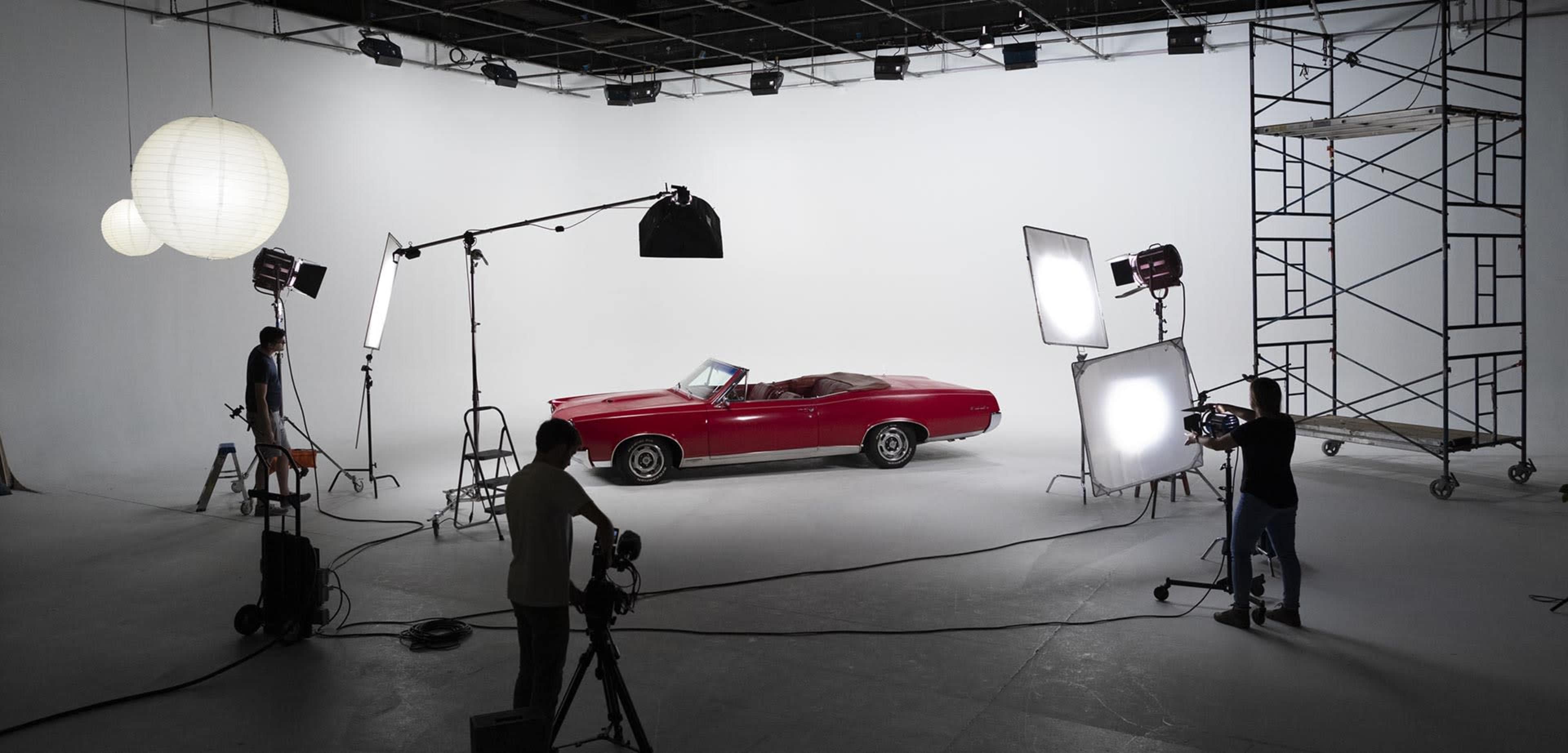 A red convertible car is positioned in a photography studio with various lights and equipment set up around it.