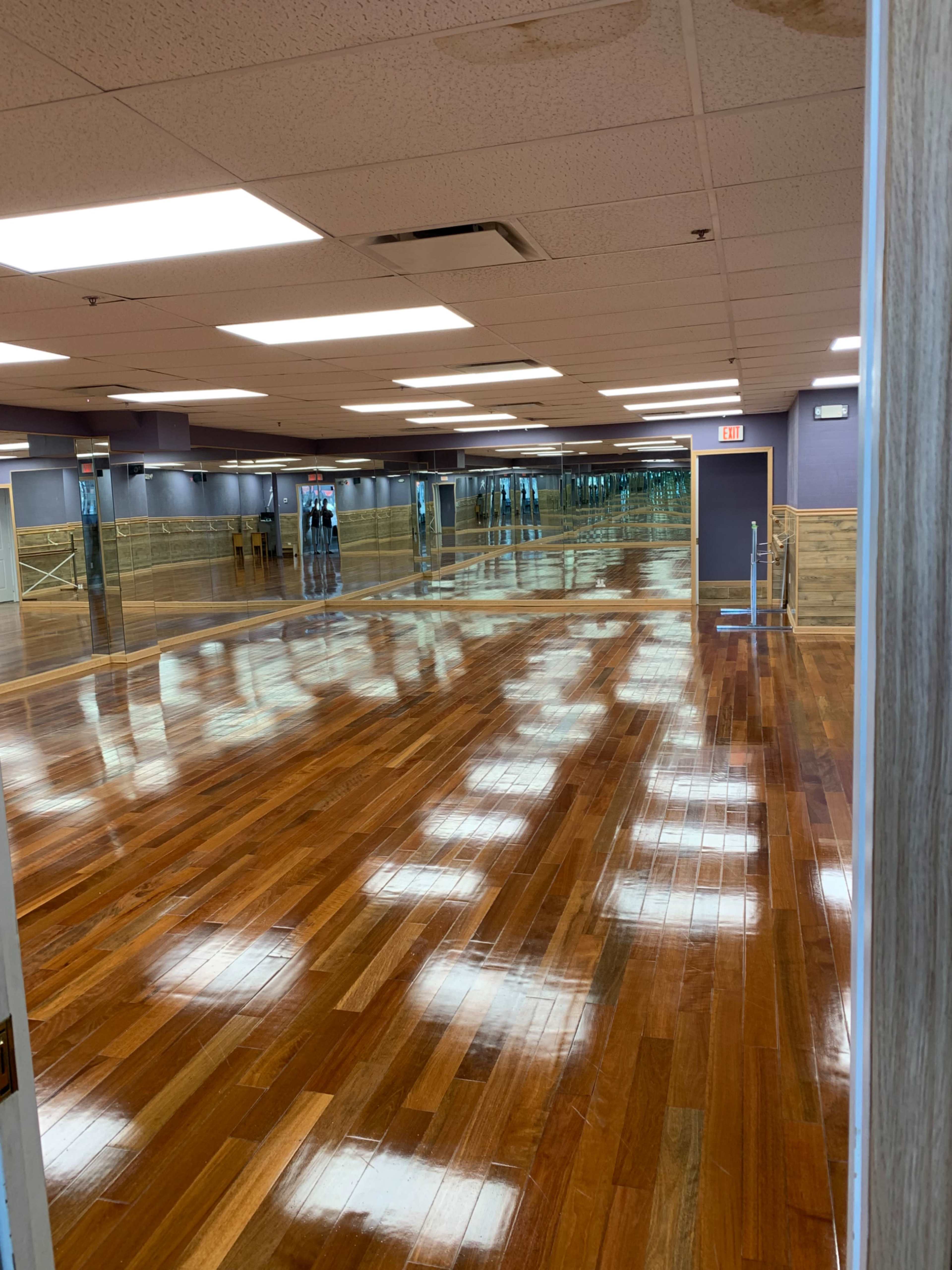 A spacious studio with polished wooden floors and mirrors lining the walls reflects overhead lighting.