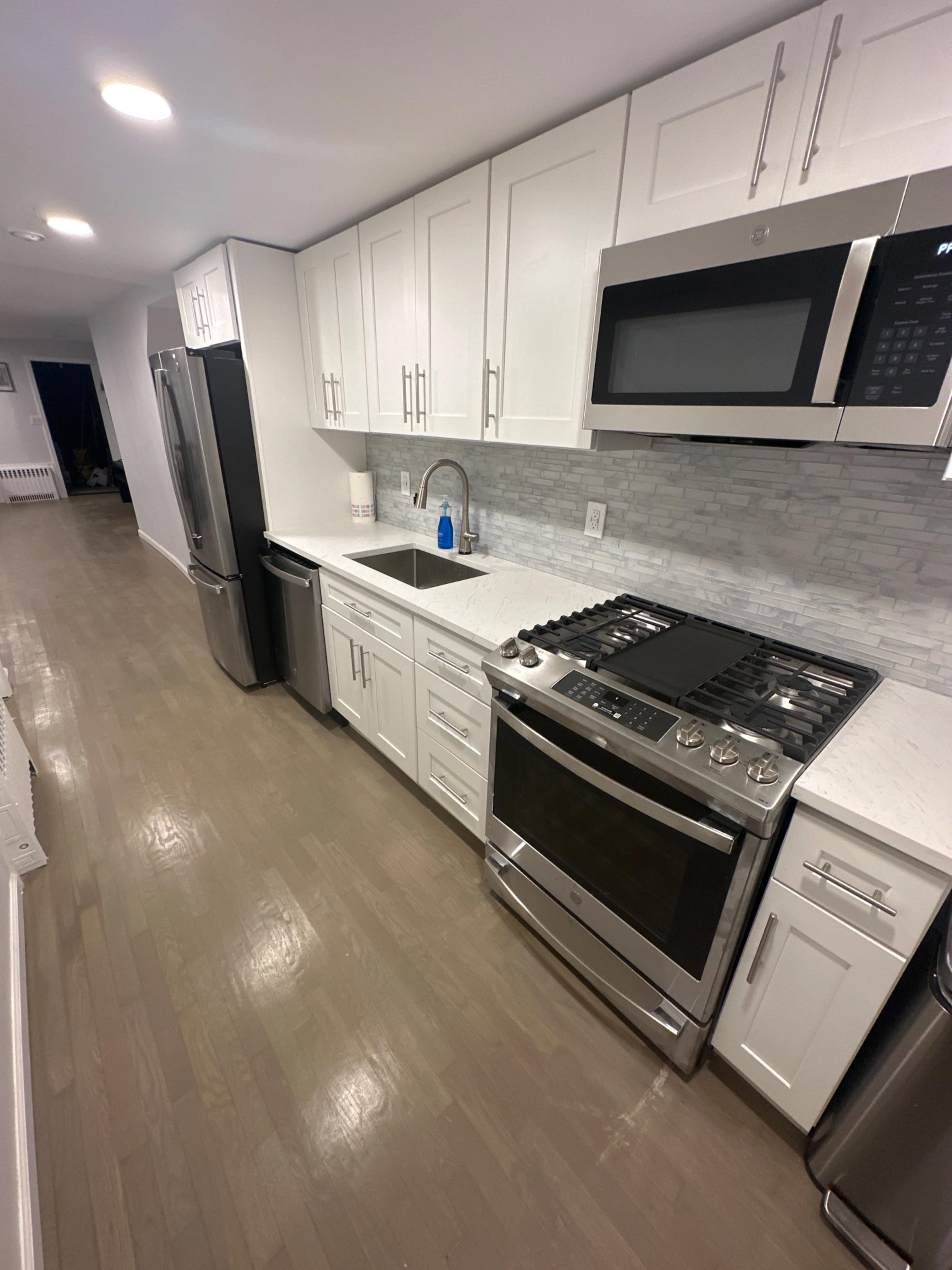 The image shows a modern kitchen with white cabinets, stainless steel appliances, and a marble countertop.