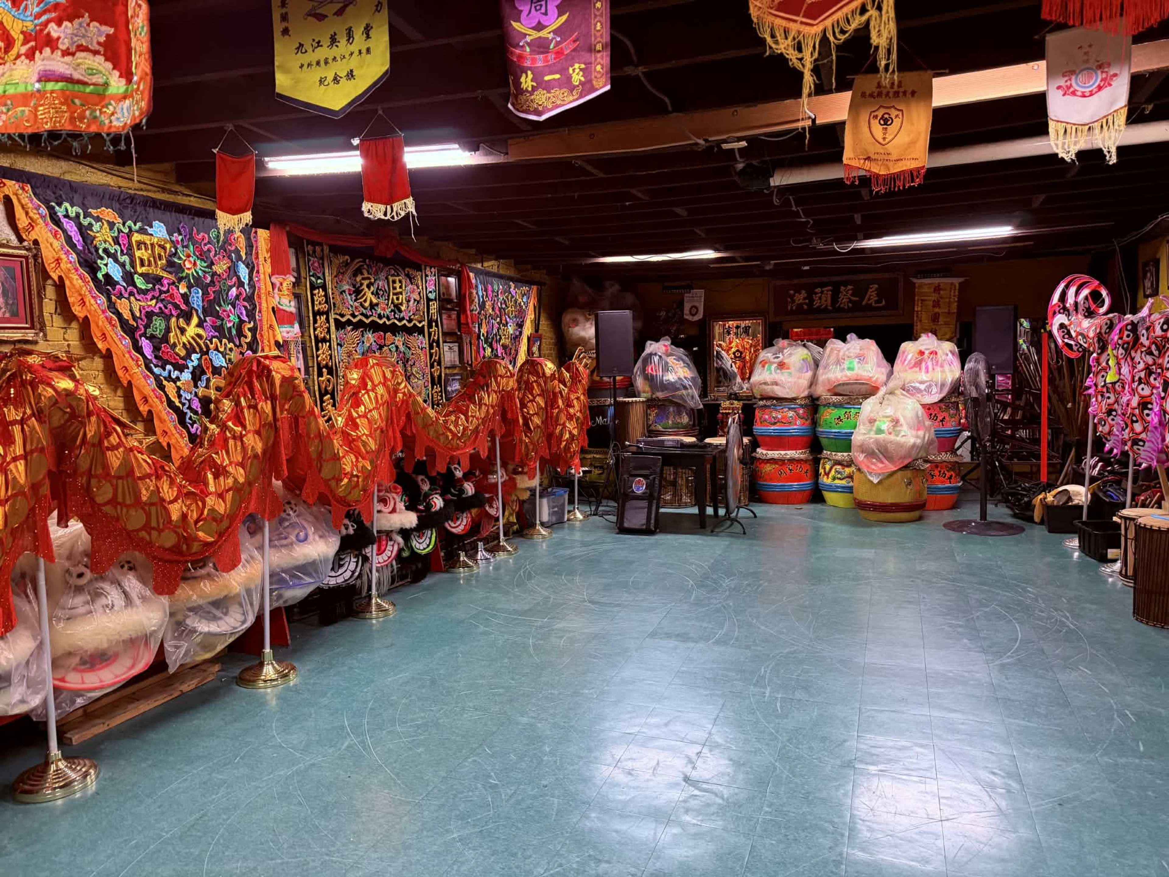 The interior of a decorated room features colorful traditional banners, ornate masks, and elaborately designed floats arranged along the walls.