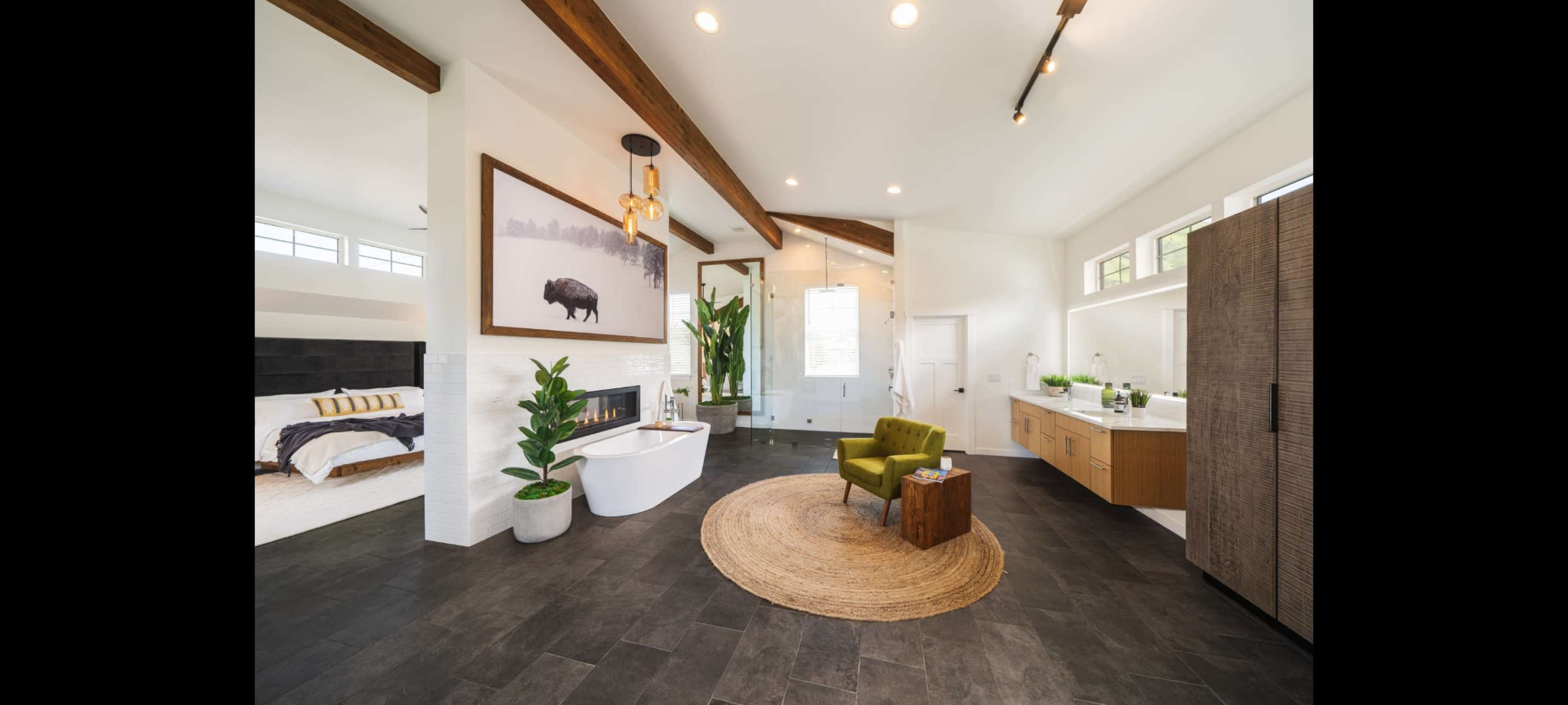 The spacious bathroom features a freestanding bathtub, a large walk-in shower, a double vanity, and modern furnishings, all highlighted by wooden beams and large windows.
