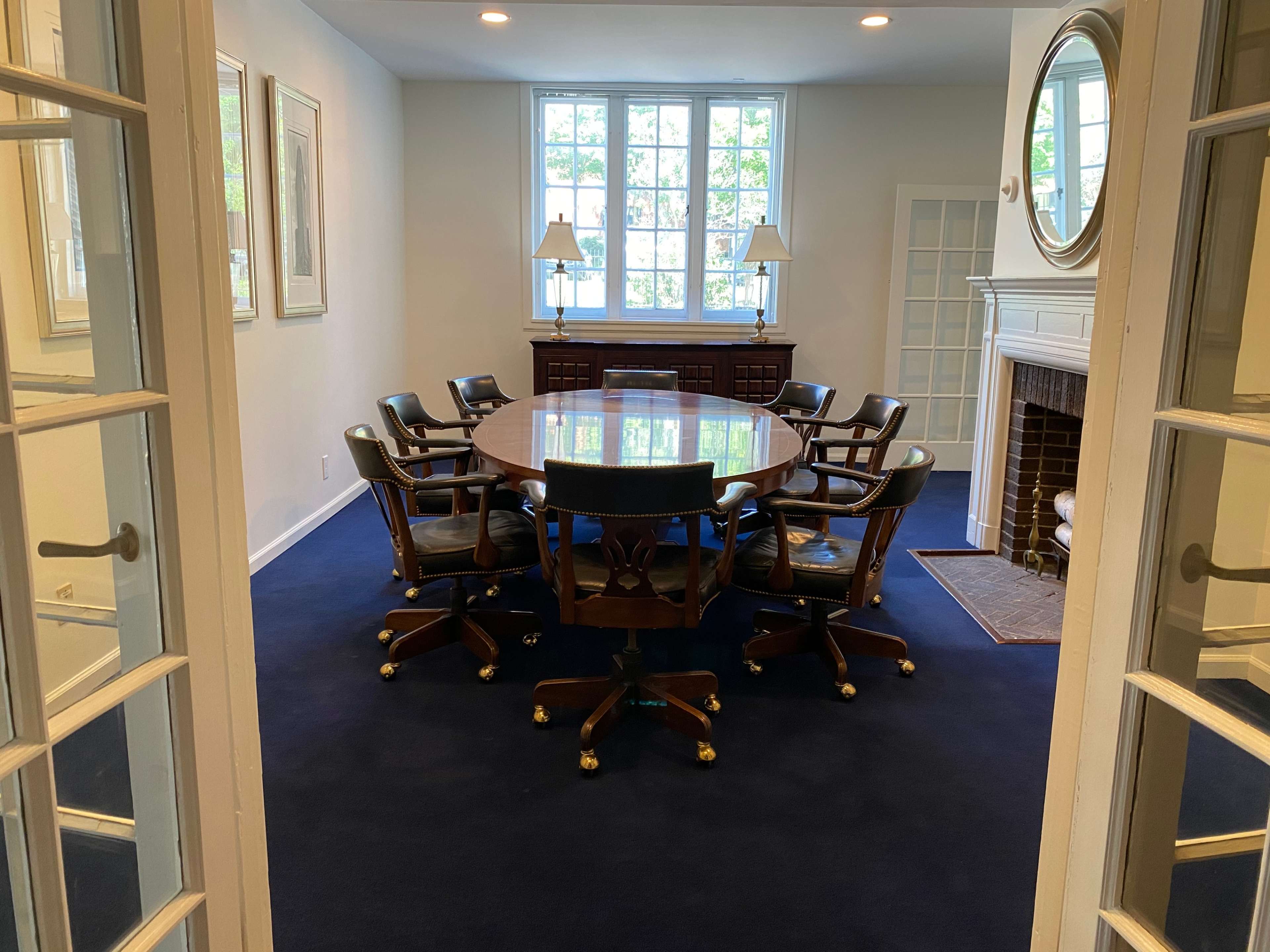 The image shows a conference room with a round table surrounded by eight chairs, framed by two sets of glass-paneled doors.