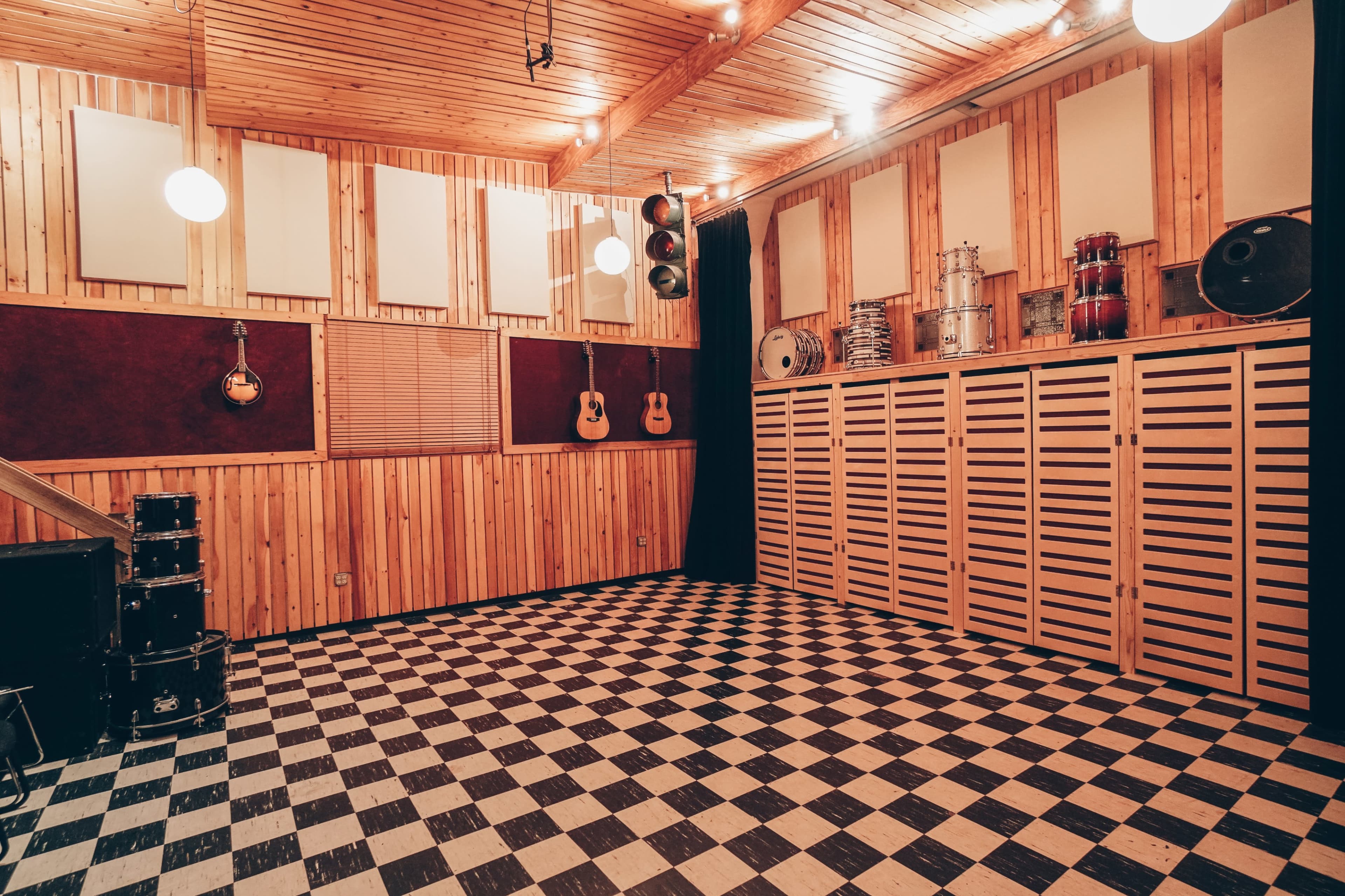 A wooden-lined recording studio with a checkered floor, featuring musical instruments and sound equipment on the walls.