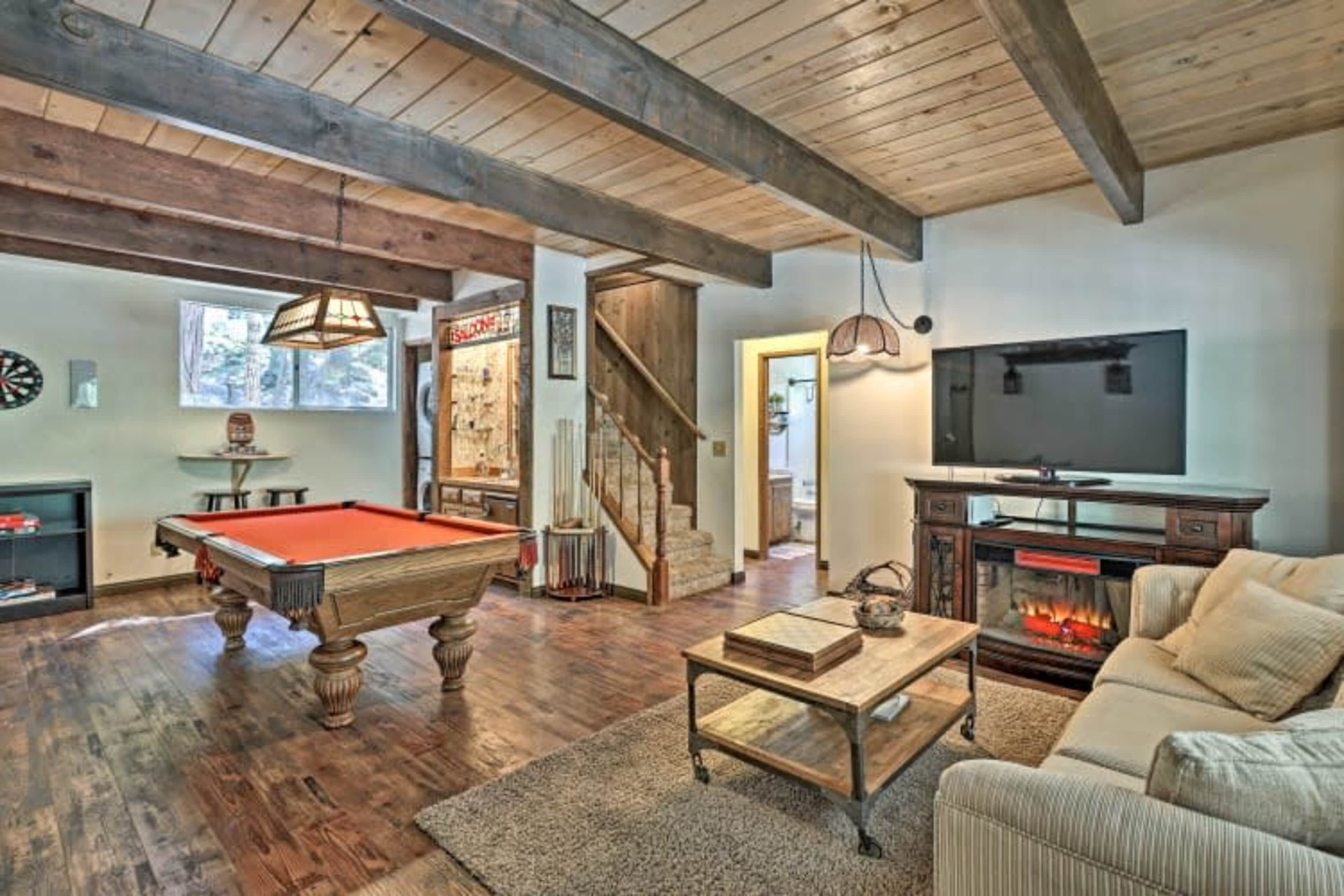 The image shows a cozy game room with a pool table, a TV mounted on the wall, a fireplace, and a comfortable seating area.