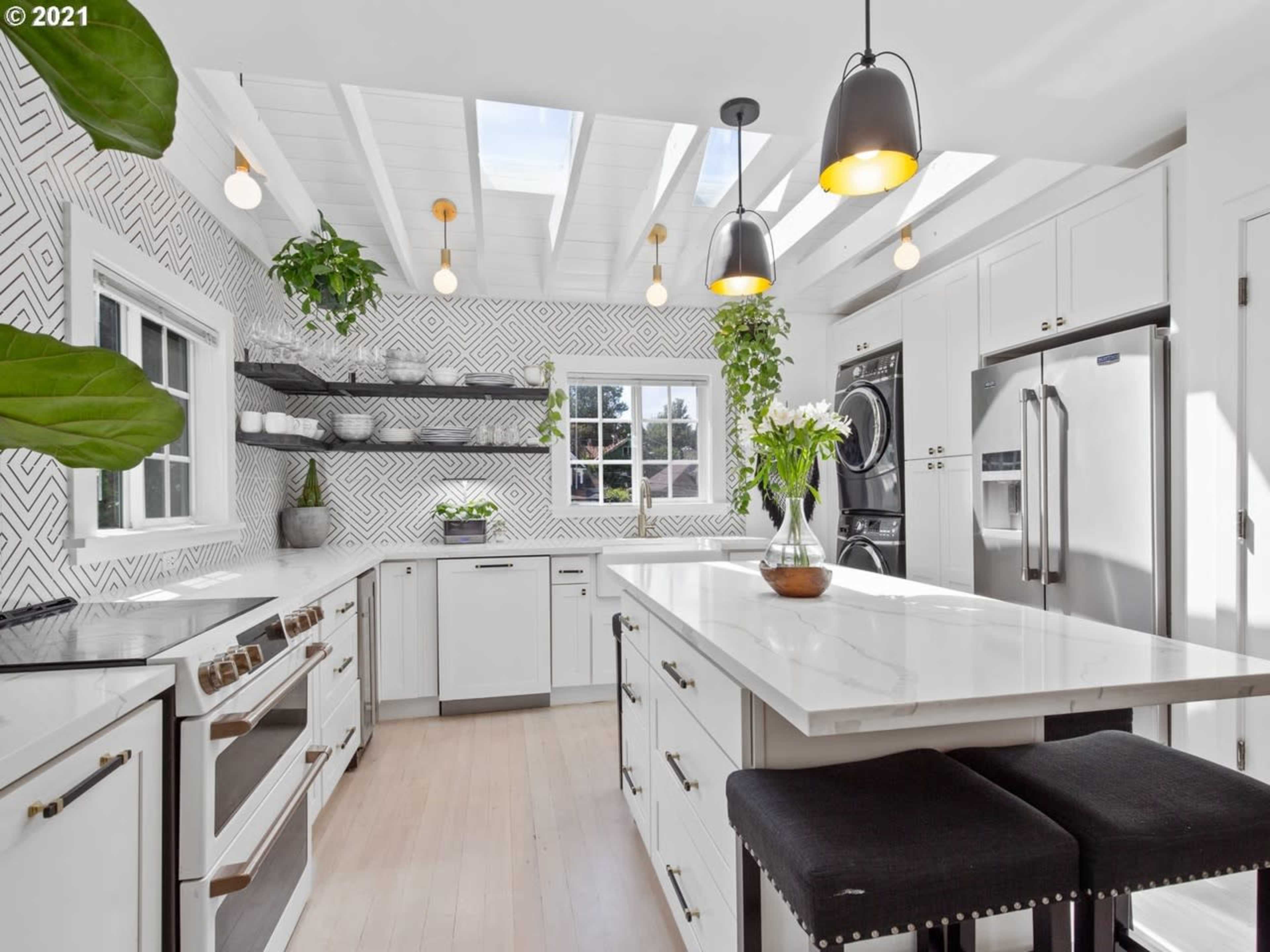 A modern kitchen features white cabinetry, a large island with a marble countertop, and geometric patterned wall tiles.