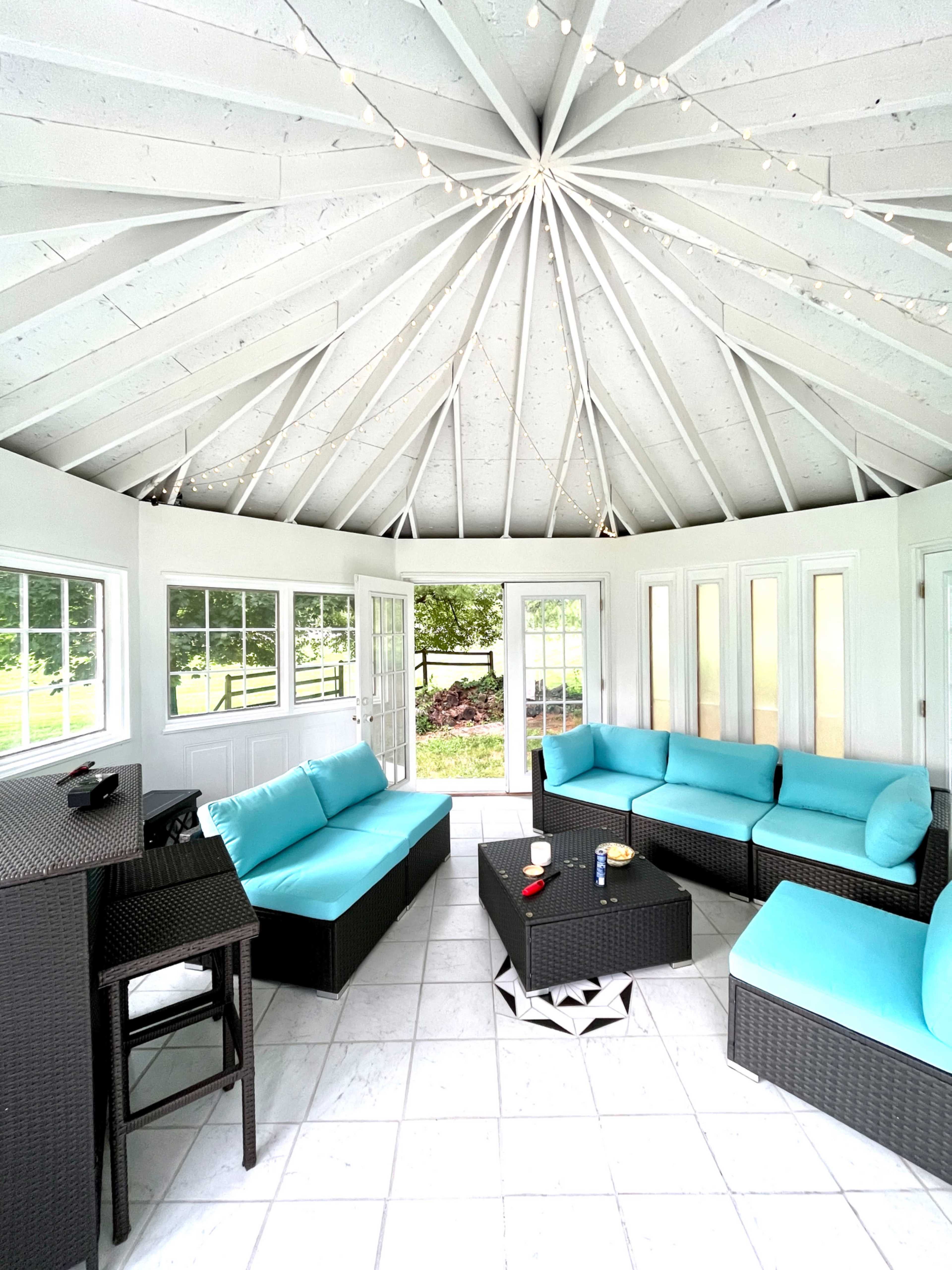 A sunroom with a circular ceiling, featuring turquoise seating and a black coffee table surrounded by large windows.