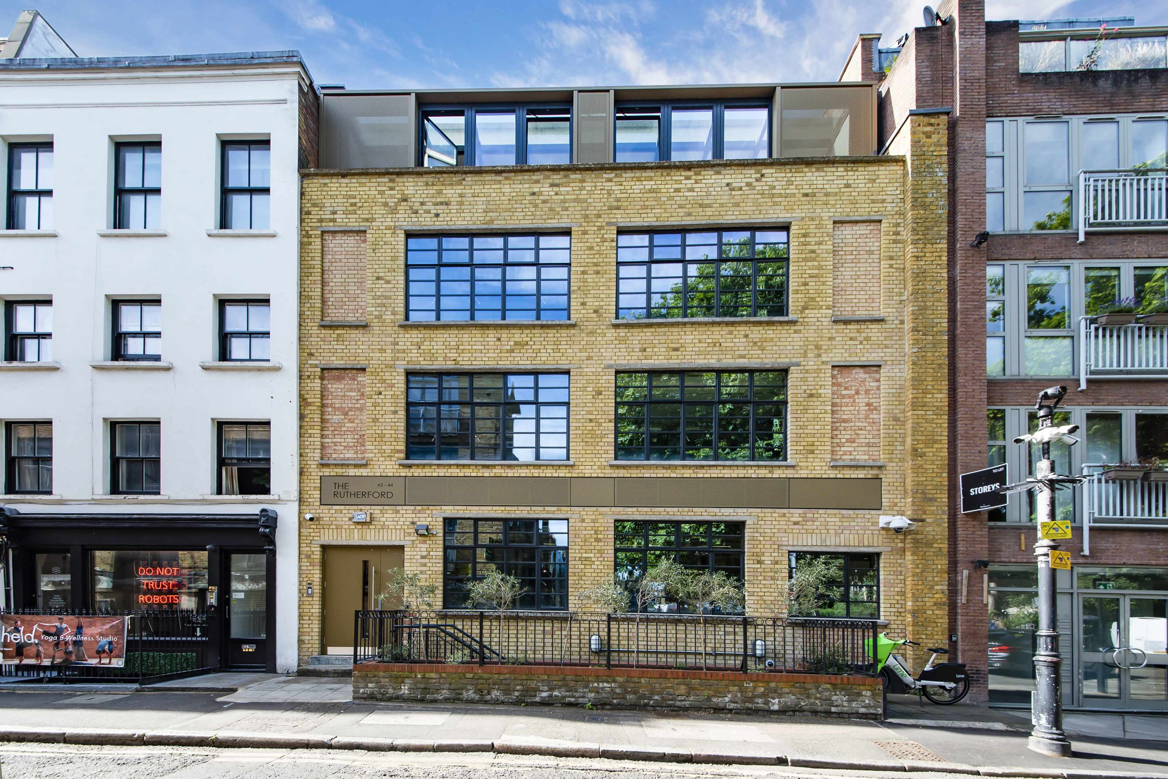 A modern yellow-brick building with large windows, situated between two other buildings in an urban setting.