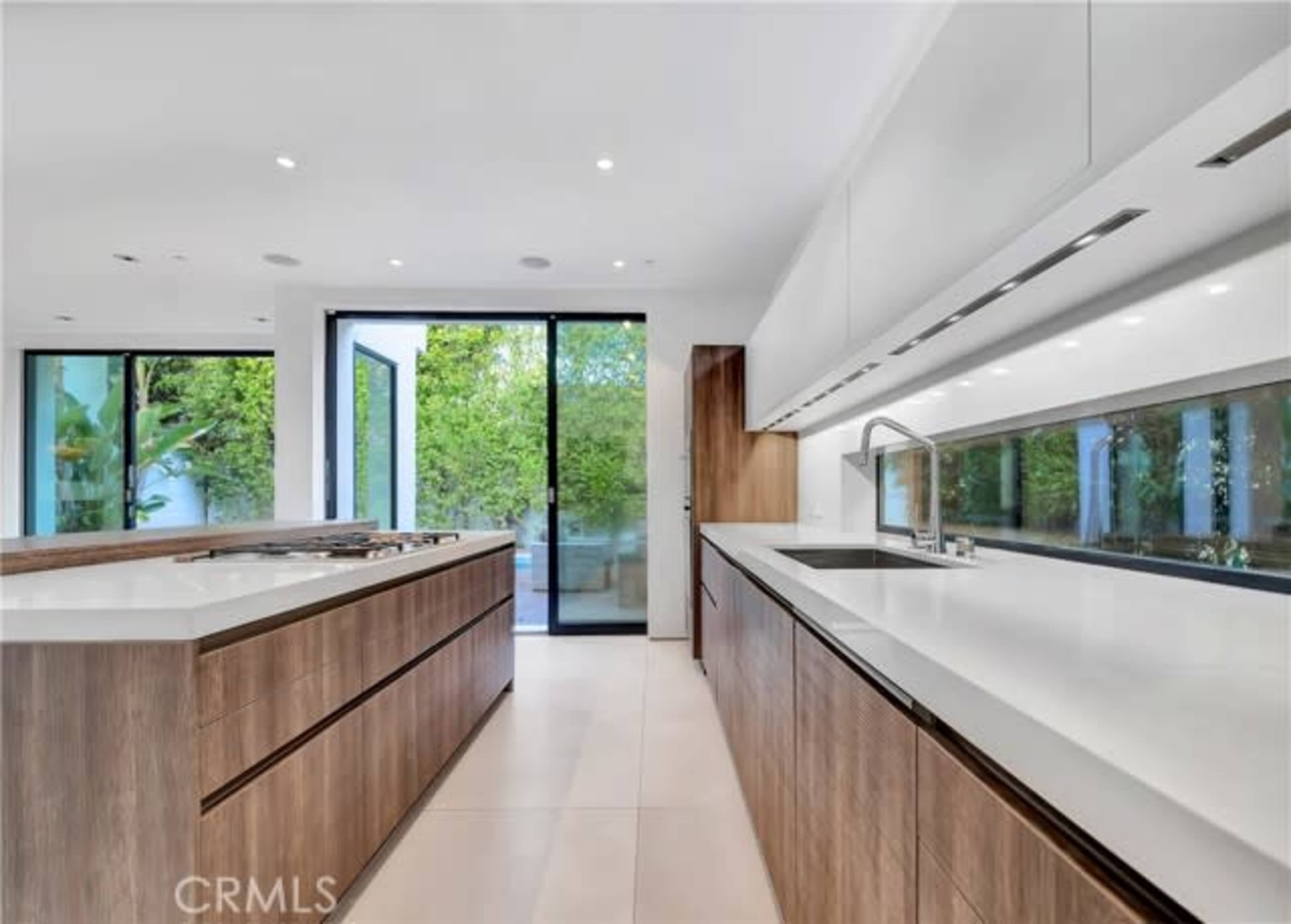 The image shows a modern kitchen with wooden cabinetry, a large island, and sliding glass doors that open to an outdoor area.