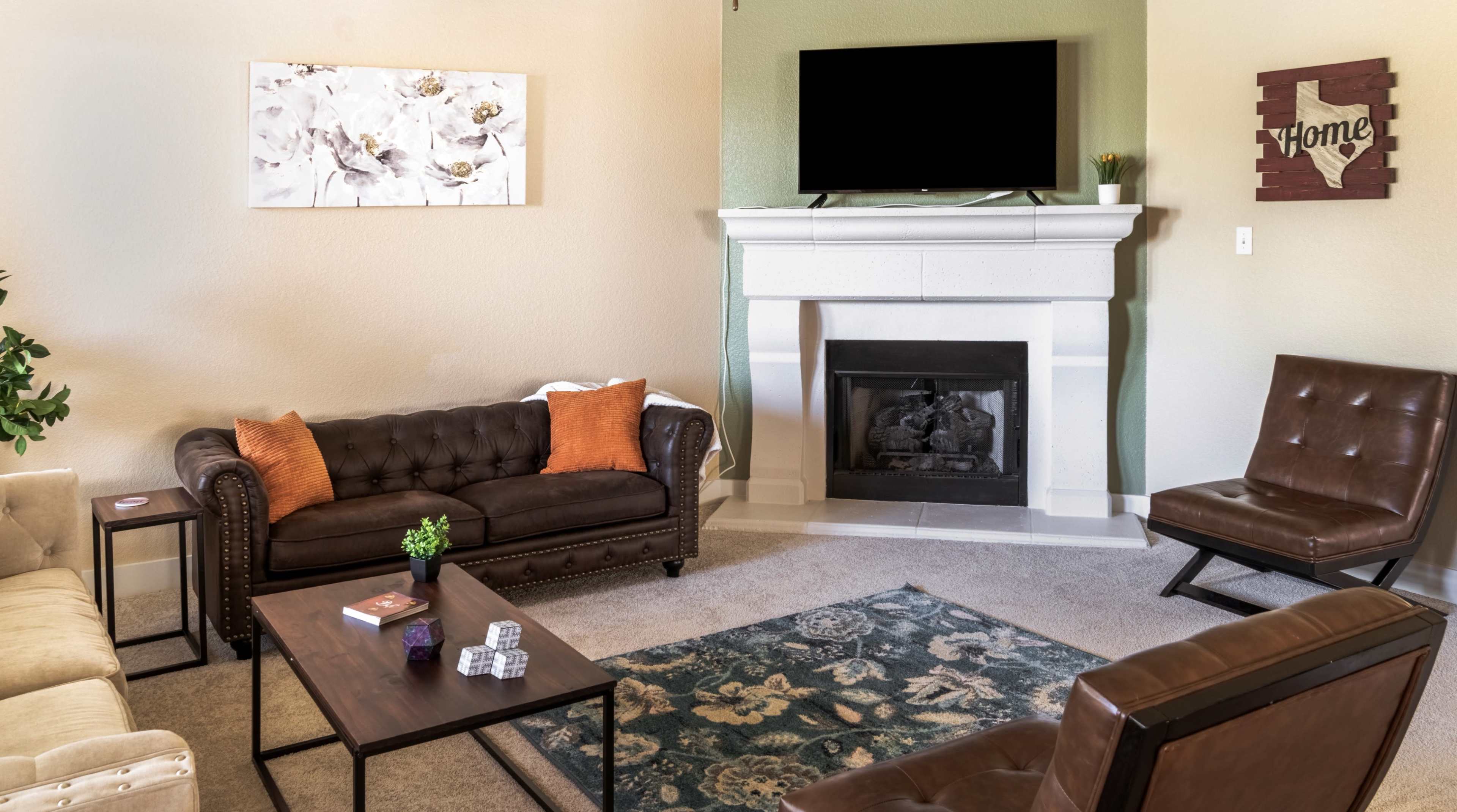 A cozy living room with a fireplace, a television mounted above it, and various seating options arranged around a coffee table.