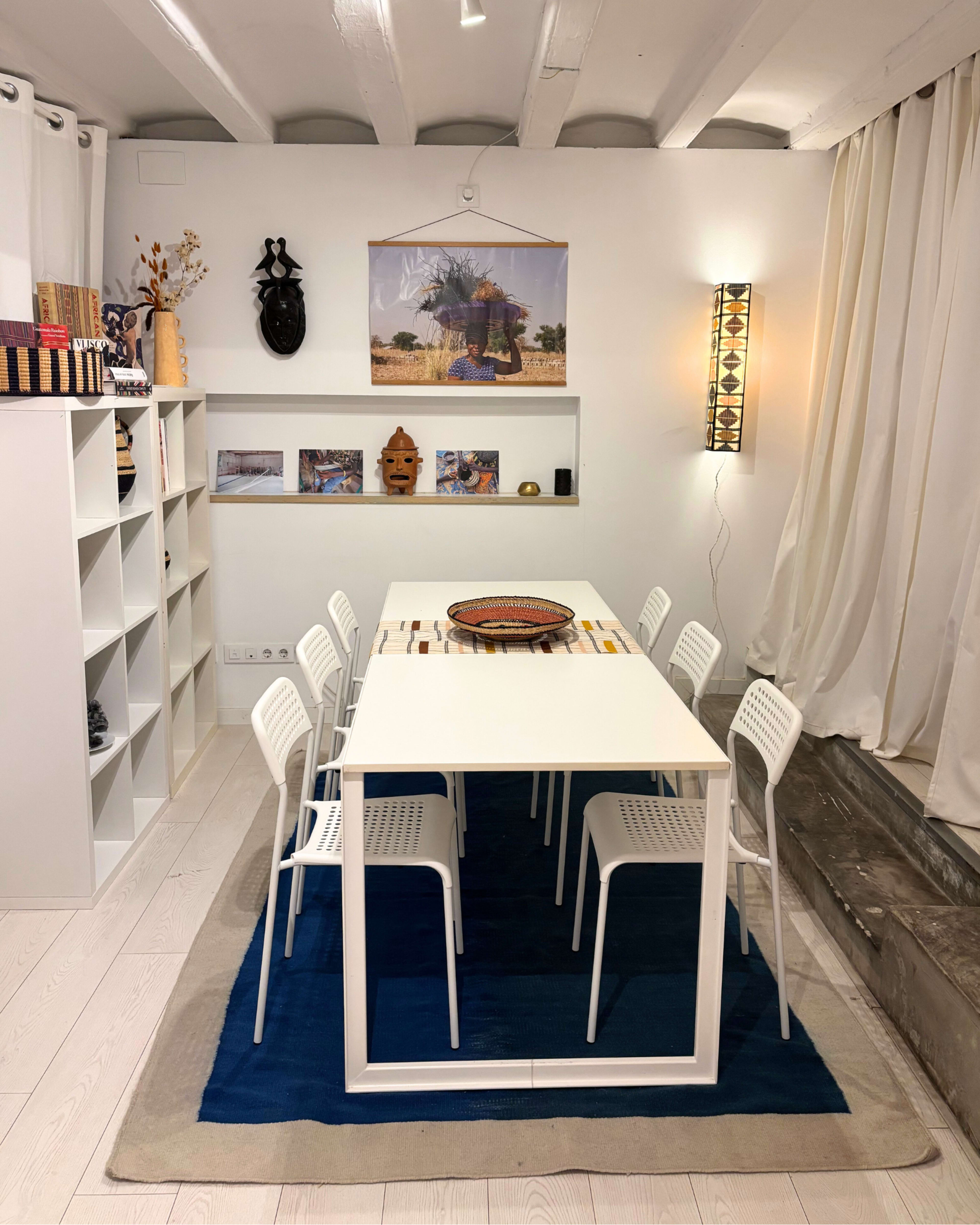 The image shows a modern dining area with a white table surrounded by white chairs, featuring decorative items on the shelves and artwork on the walls.