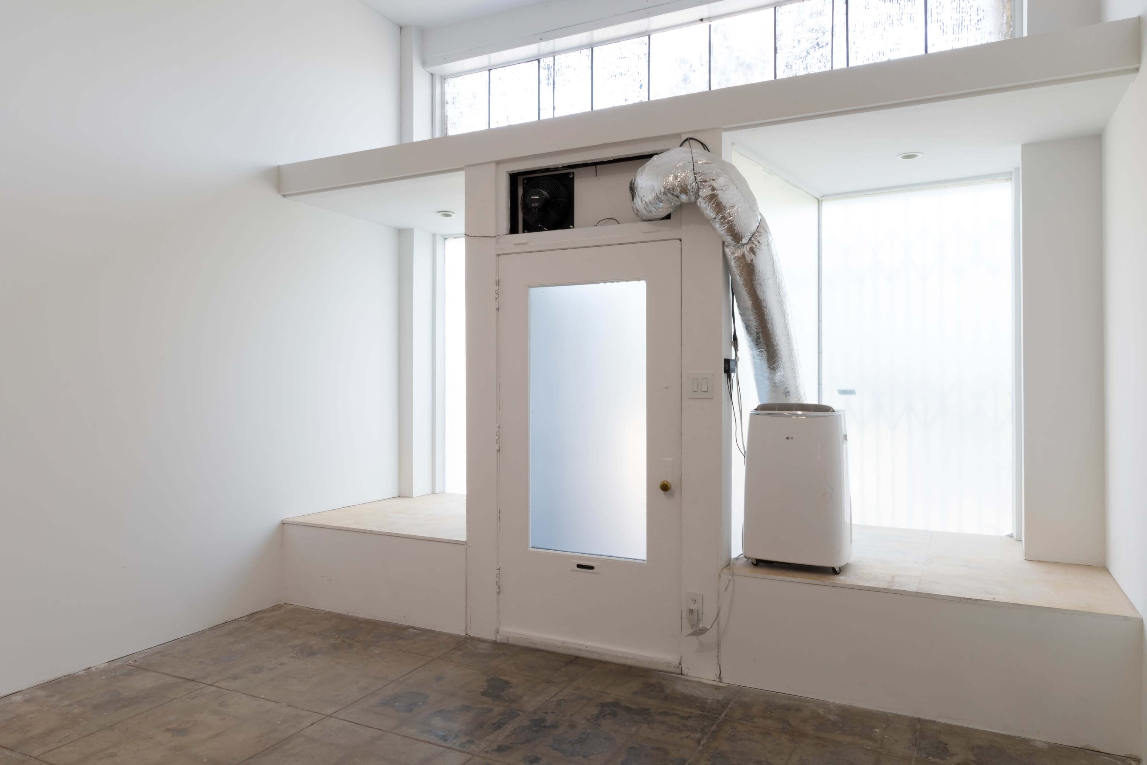 A minimalist interior space with a white wall, a door featuring a frosted glass panel, and an air conditioning unit connected by a duct.