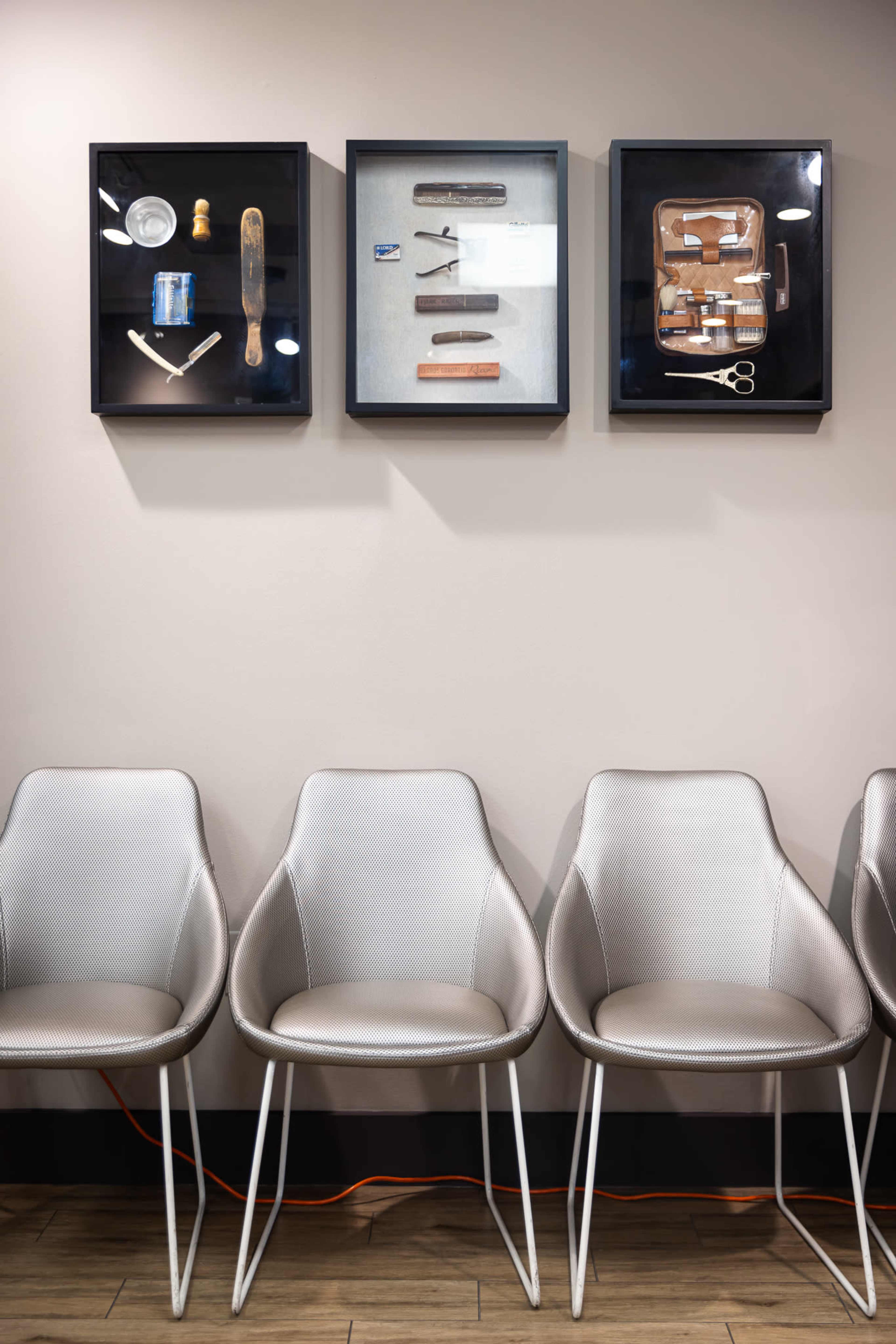The image depicts a row of sleek, modern chairs beneath two framed displays of various grooming tools on a wall.