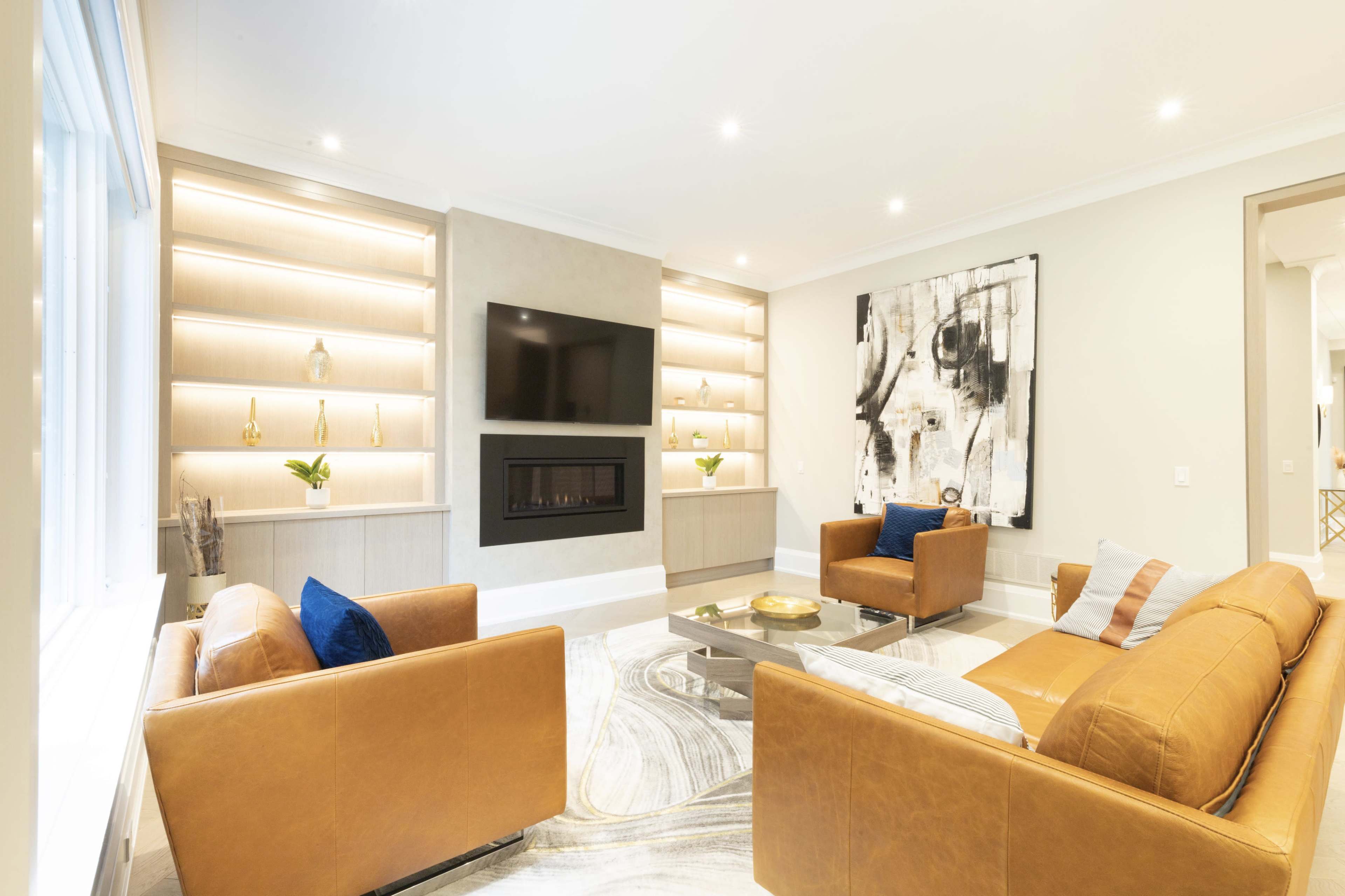 A modern living room featuring two leather sofas, a mounted TV above a fireplace, and minimalist shelves with decor.