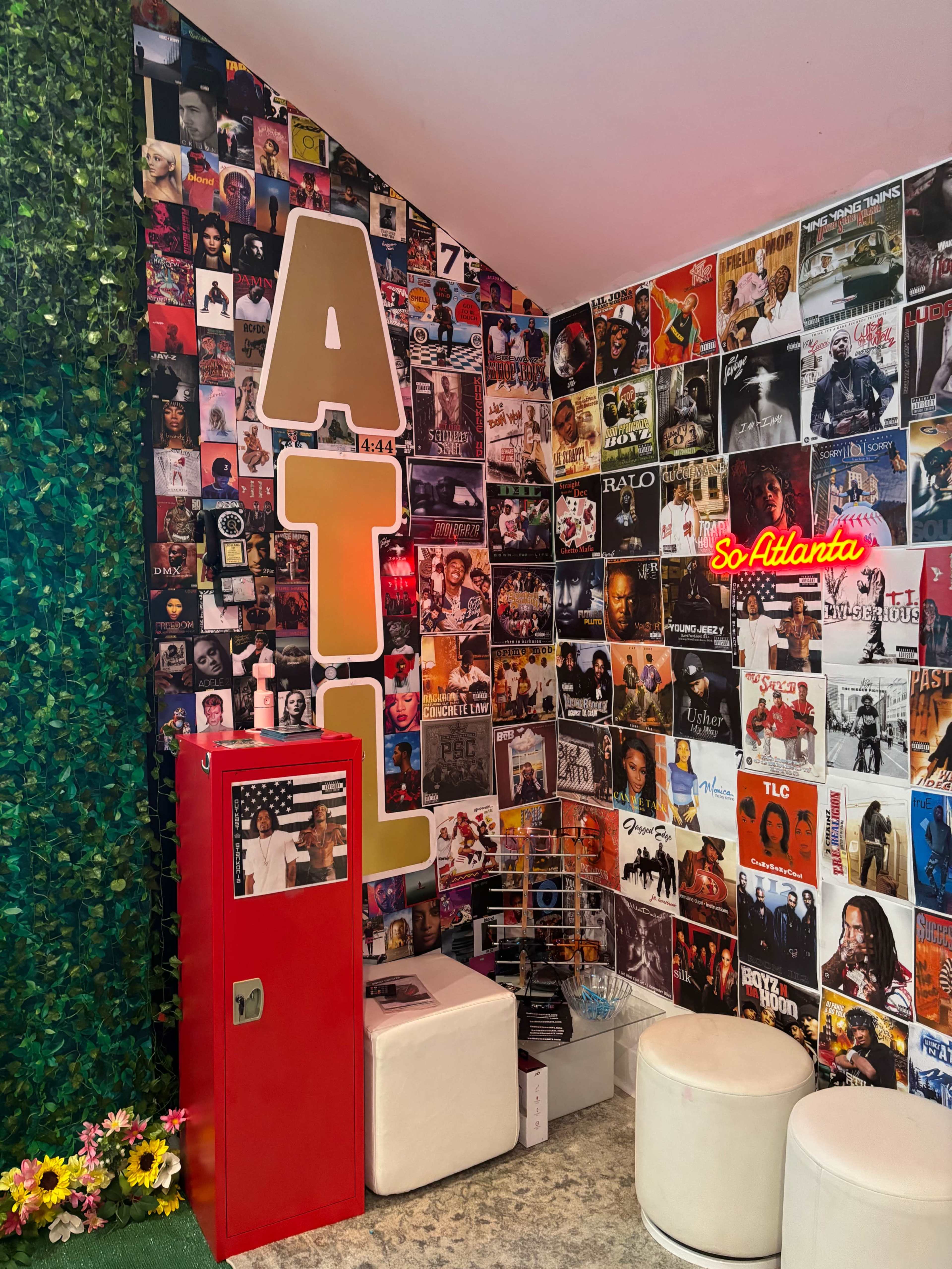The scene features a corner room decorated with a collage of album covers on the walls, a bright red retro phone booth, and seating on white stools, with the letter "ATL" prominently displayed.