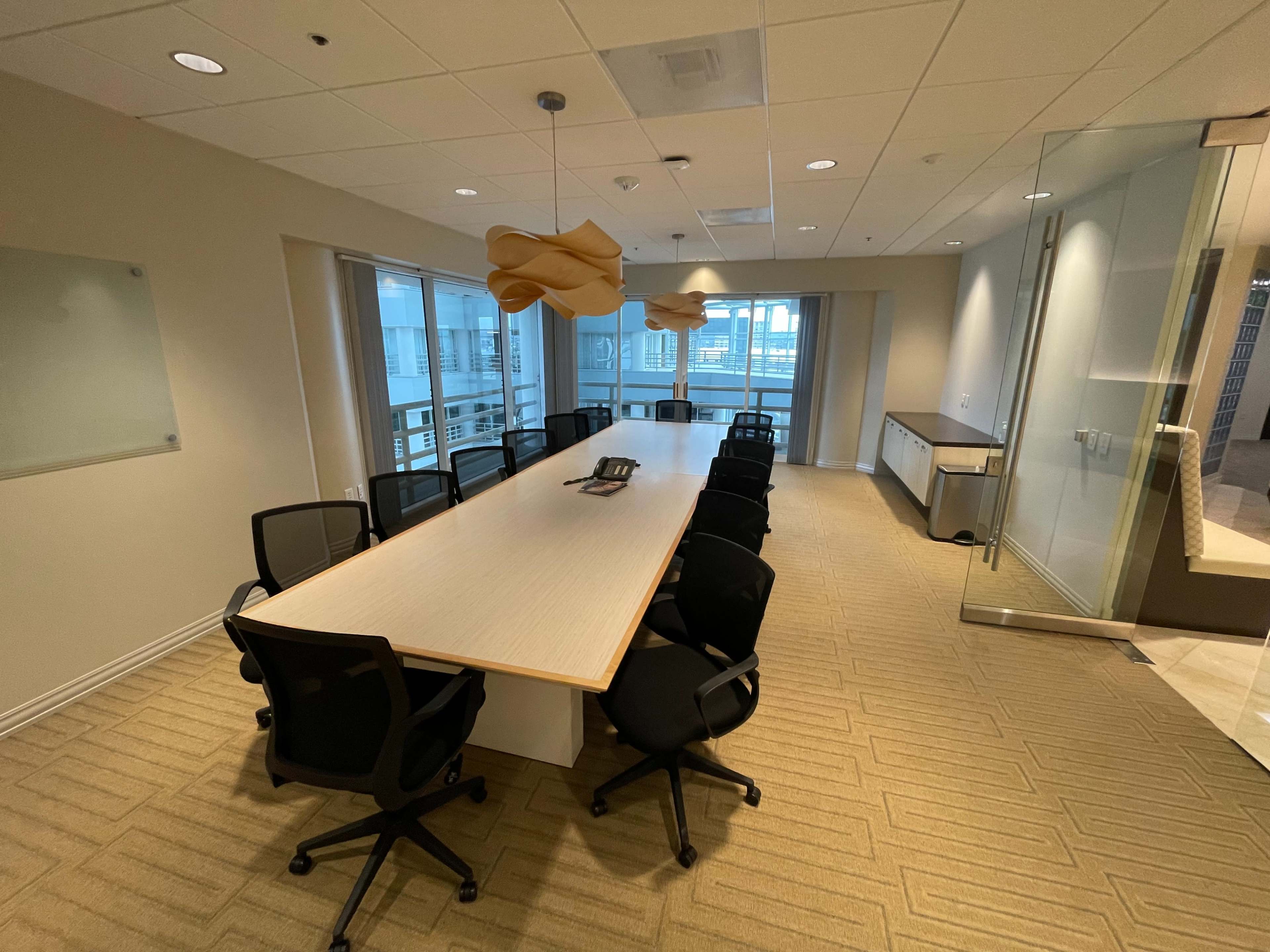 The image shows a conference room with a long table surrounded by black office chairs and two pendant lights hanging above.